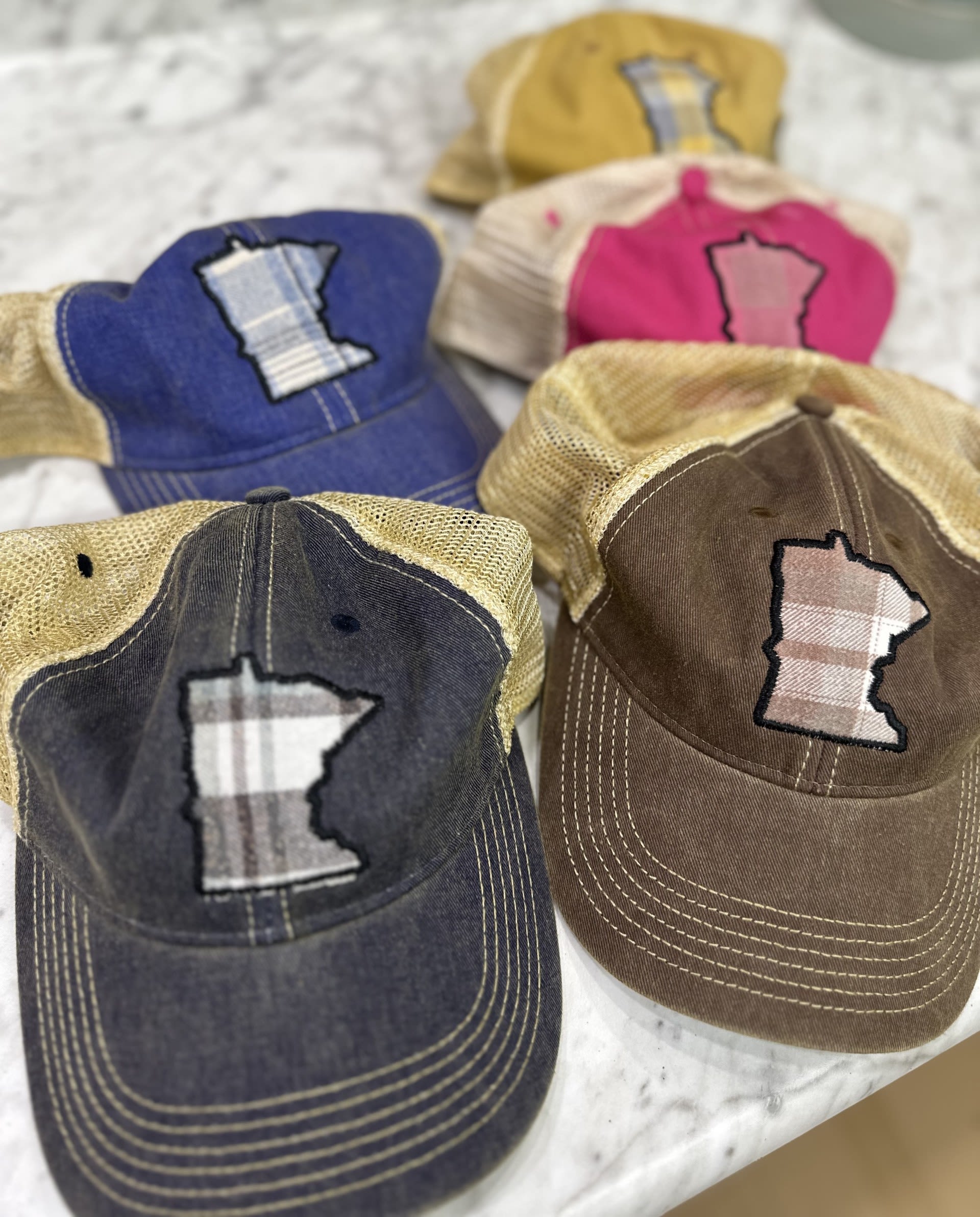 Four baseball caps with Minnesota-shaped patches arranged on a light surface.