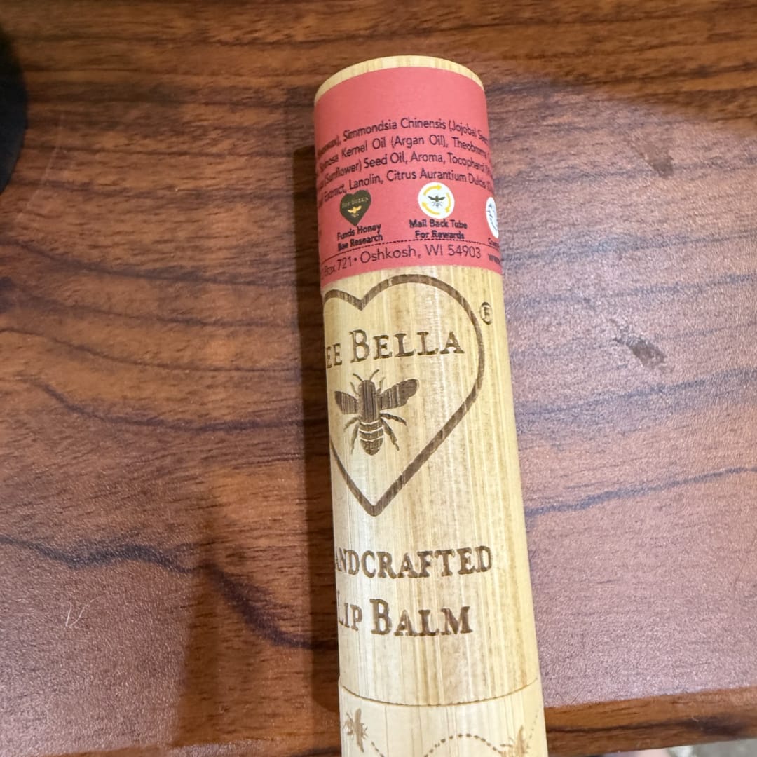 A tube of Bee Bella handcrafted lip balm on a wooden surface.