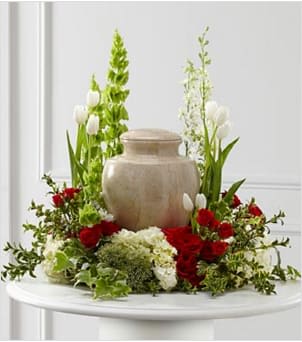 The FTD® Tears of Comfort™ Arrangement - The FTD® Tears of Comfort™ Arrangement is an elegant and sophisticated way to surround their urn with floral beauty at the final farewell service. Rich red roses and spray roses are vivid and bright amongst white tulips, larkspur, hydrangea and trachelium, accented with the bright greens of Bells of Ireland, hypericum berries, ivy and myrtle, creating a wonderful way to honor the life of the deceased.  Approximately 21"H x 24"W. Your purchase includes a complimentary personalized gift message.