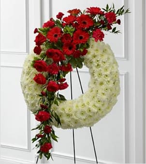 The FTD® Graceful Tribute™ Wreath - The FTD® Graceful Tribute™ Wreath creates a stunning presentation of love's serenity for their final farewell service. Red roses, carnations and gerbera daisies are accented with burgundy mini carnations and a variety of lush greens to create a sweeping arrangement that glides across the face of a snow white wreath consisting of chrysanthemums making this a remembrance for one who has touched your life like none other. Displayed on a wire easel. Approximately 58"H x 27"W. Your purchase includes a complimentary personalized gift message.