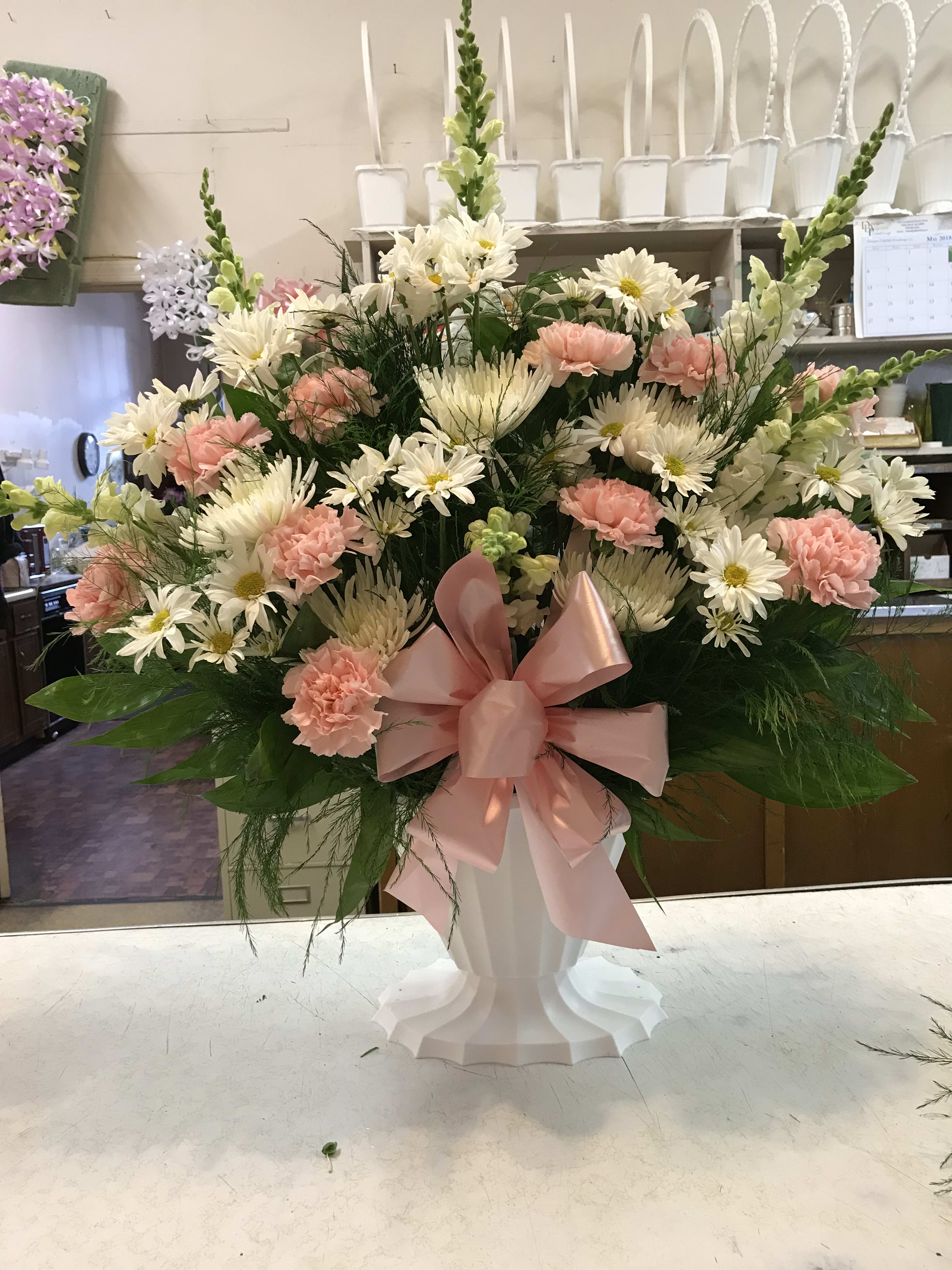 Pink and white mixed flower arrangement in a white pedestal vase with a pink bow