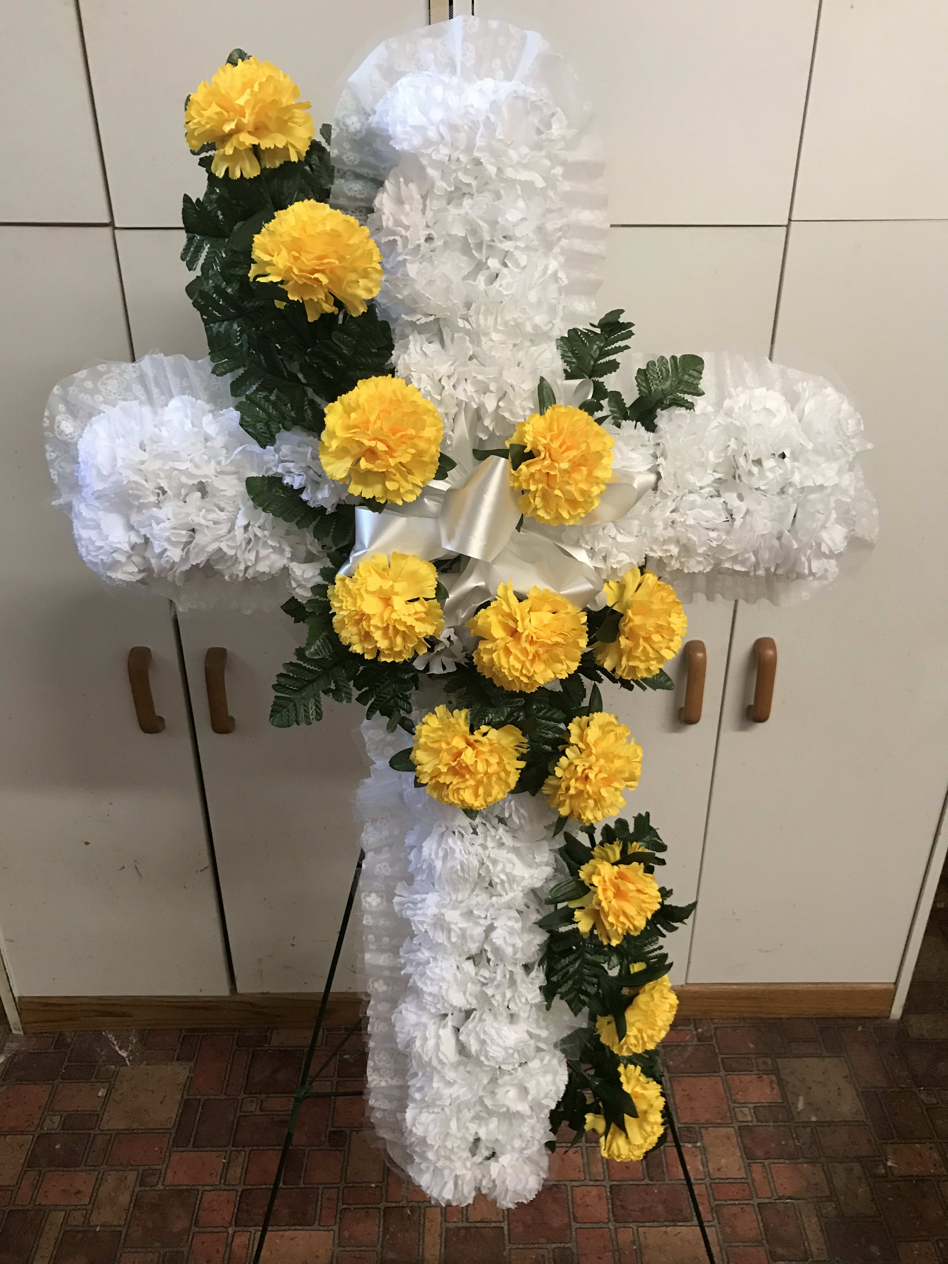 White floral cross with yellow flowers on an easel