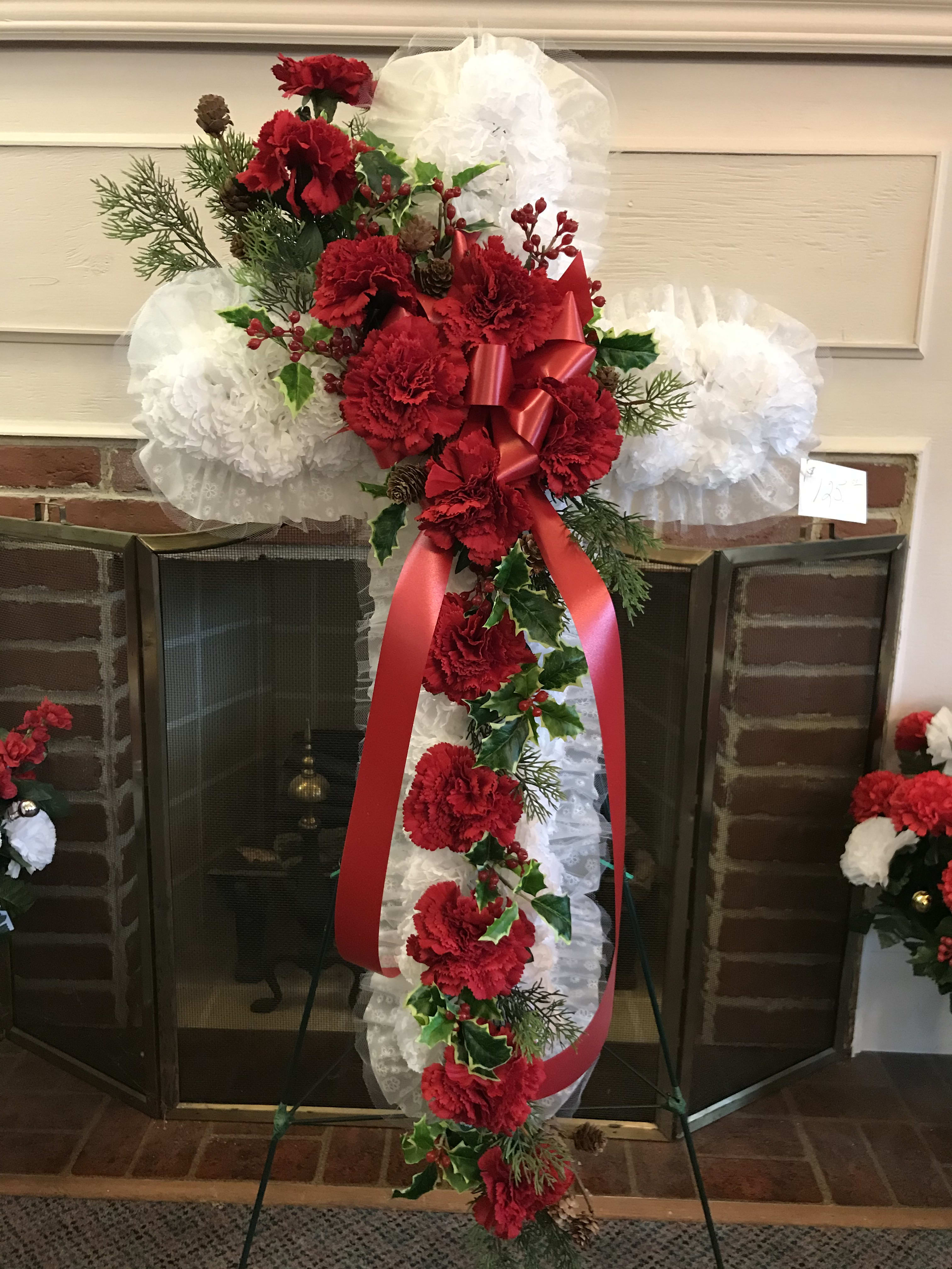 Tall red carnation funeral spray with white ruffles and a red ribbon on an easel