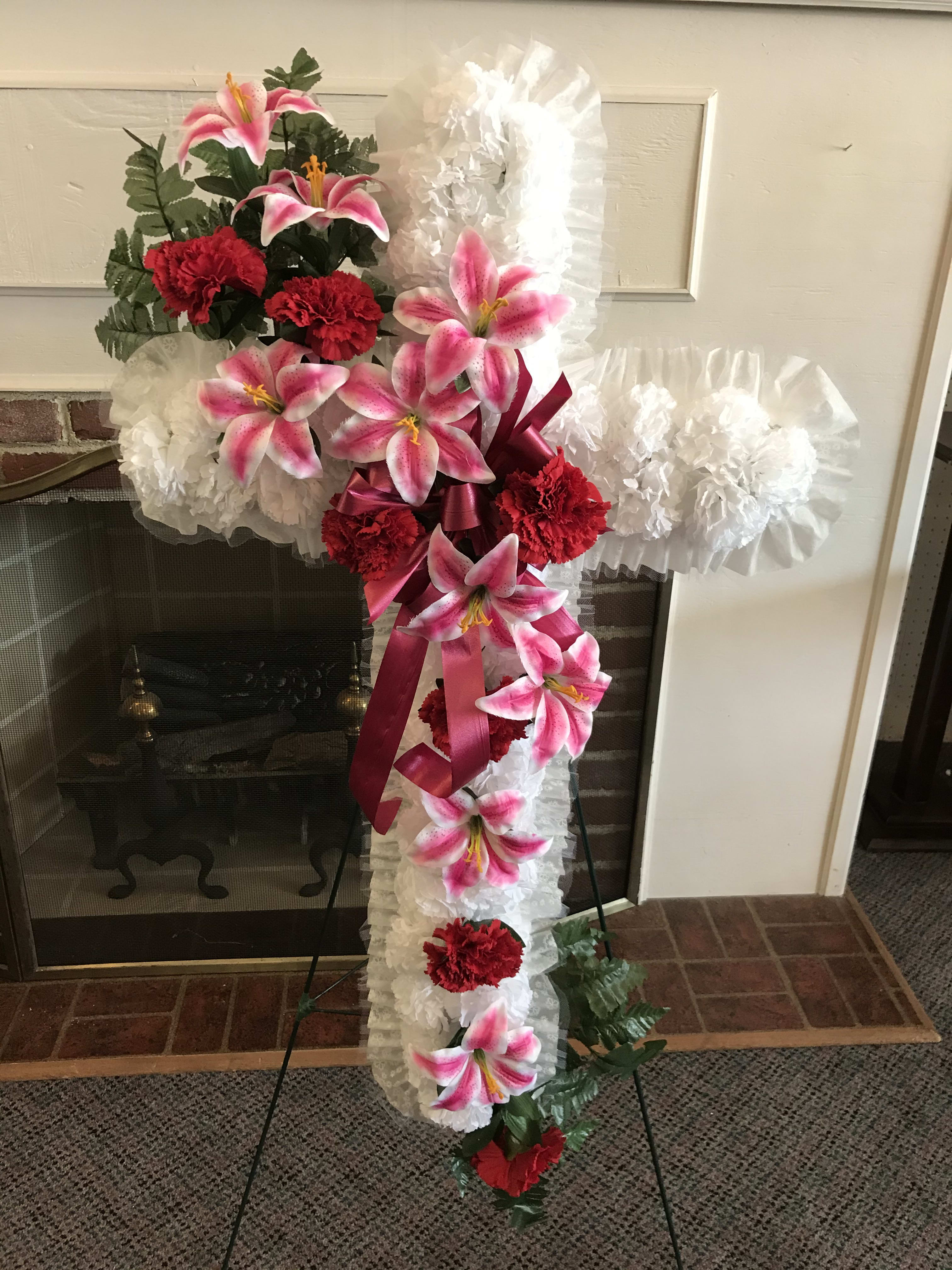 Standing floral cross with pink lilies, red carnations, and white ruffles