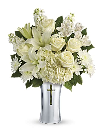 White lilies and roses arranged in a silver vase with a cross