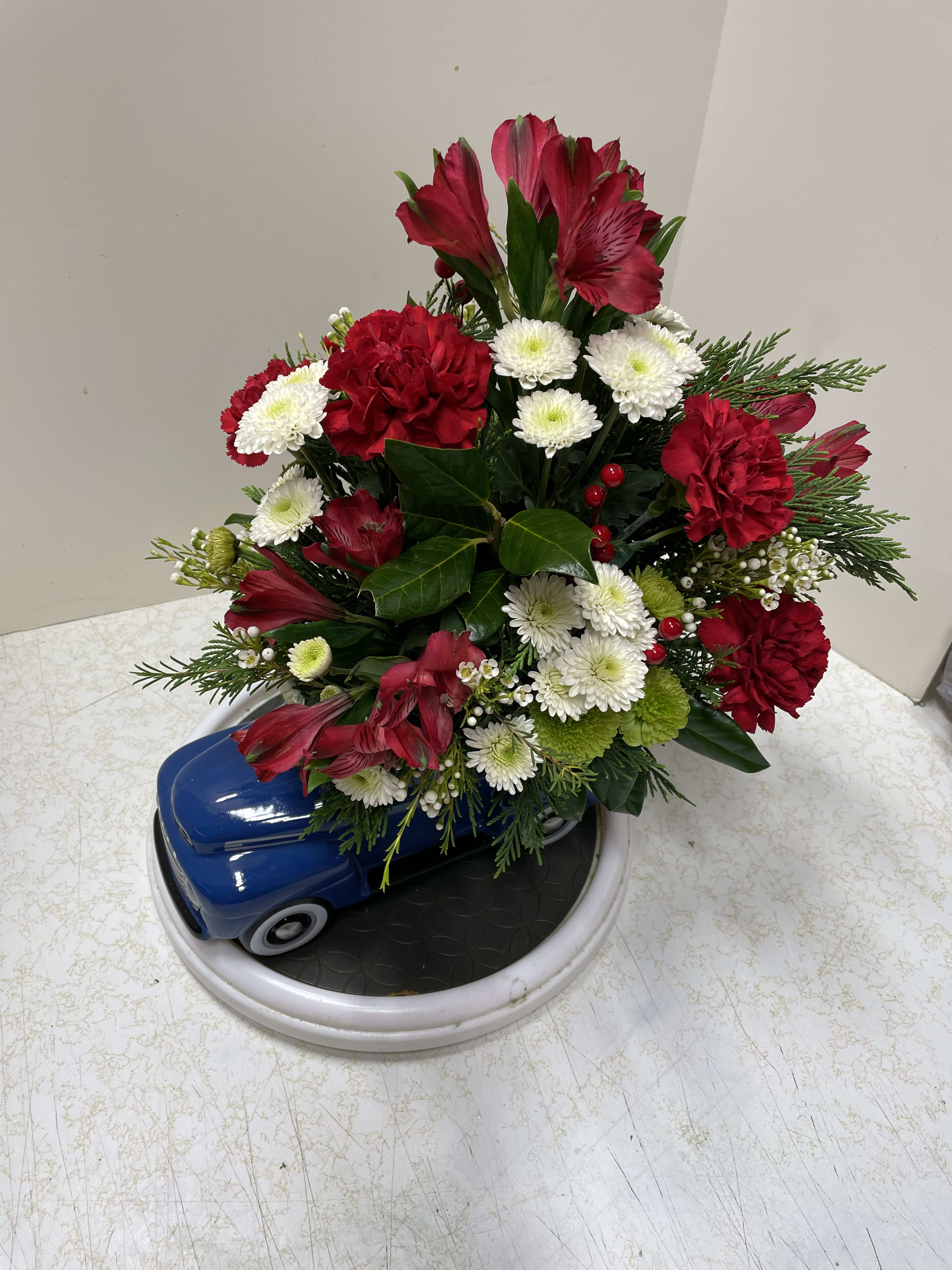 Red and white floral arrangement in a blue car-shaped container