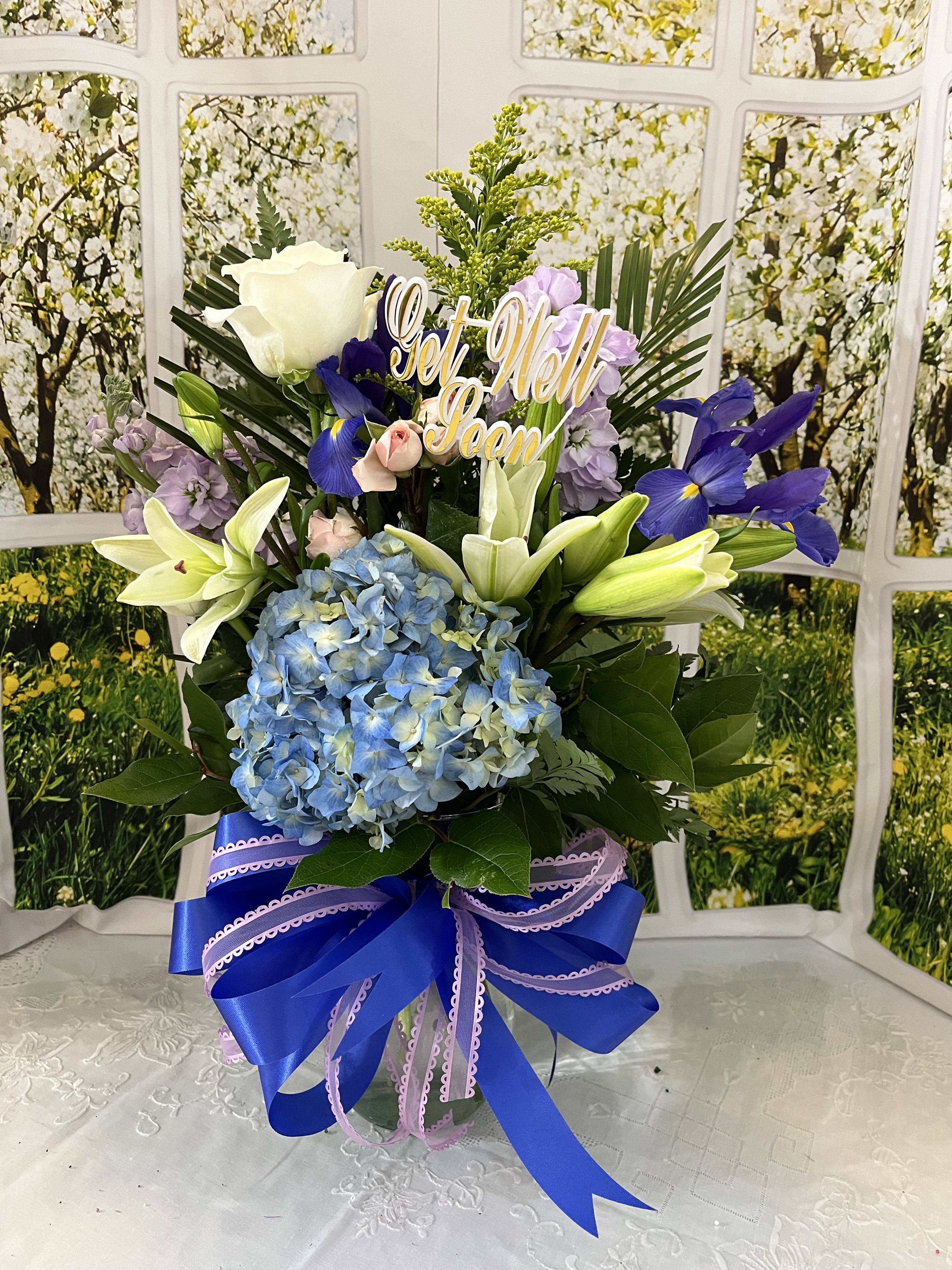 Tall floral arrangement with lilies, hydrangea, and a "Get Well Soon" sign