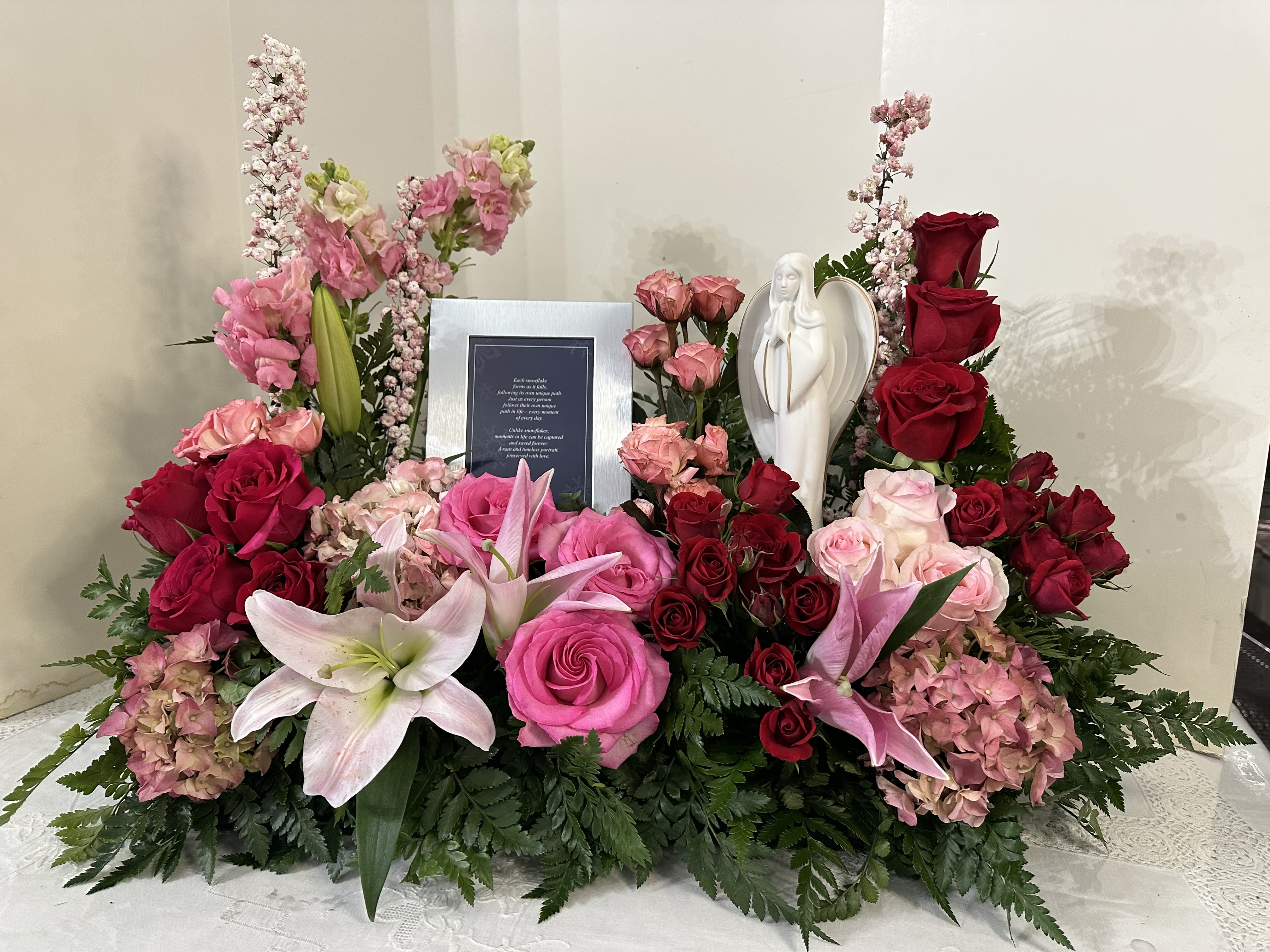 Large floral sympathy arrangement with pink and red roses, lilies, and an angel figurine