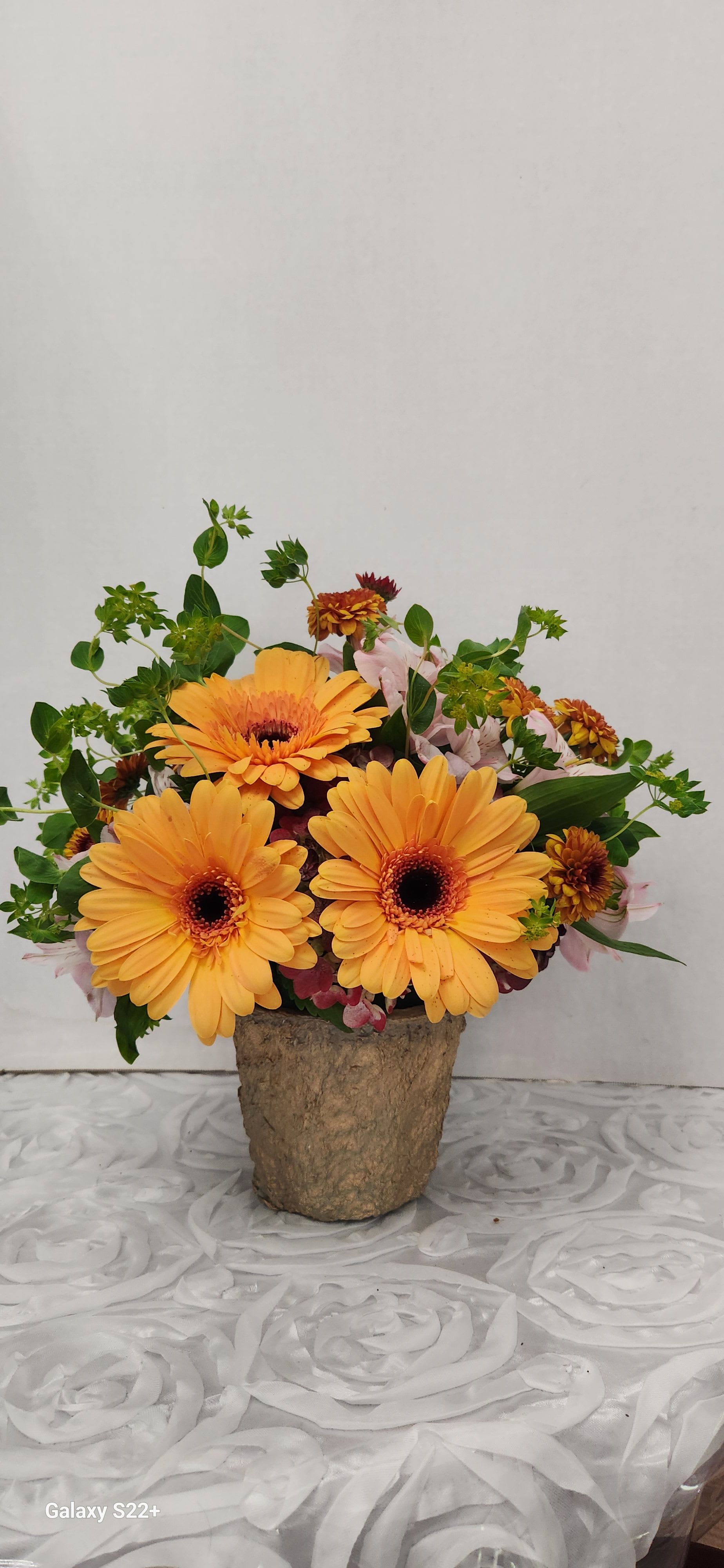 Orange gerbera daisies in a rustic vase with pink accent flowers