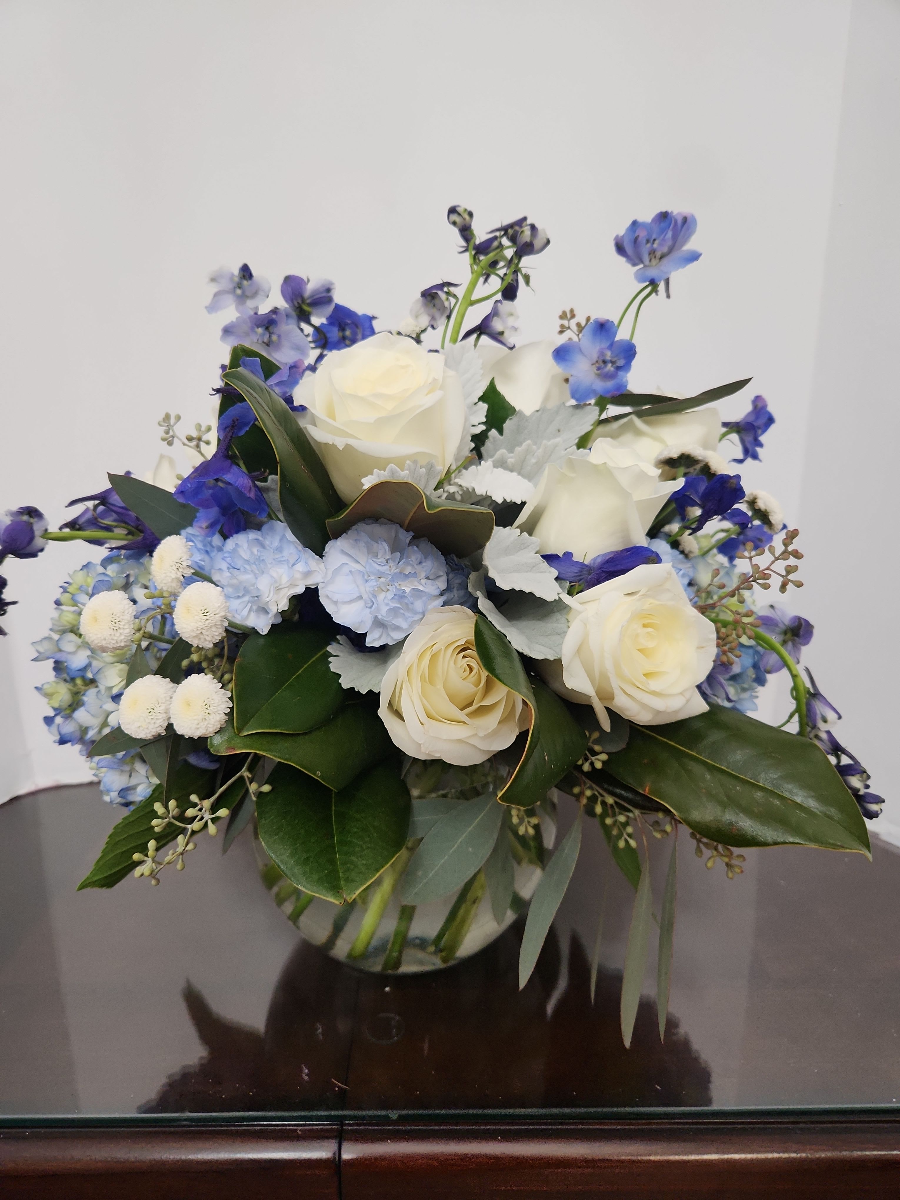White roses and blue flowers arranged in a glass vase