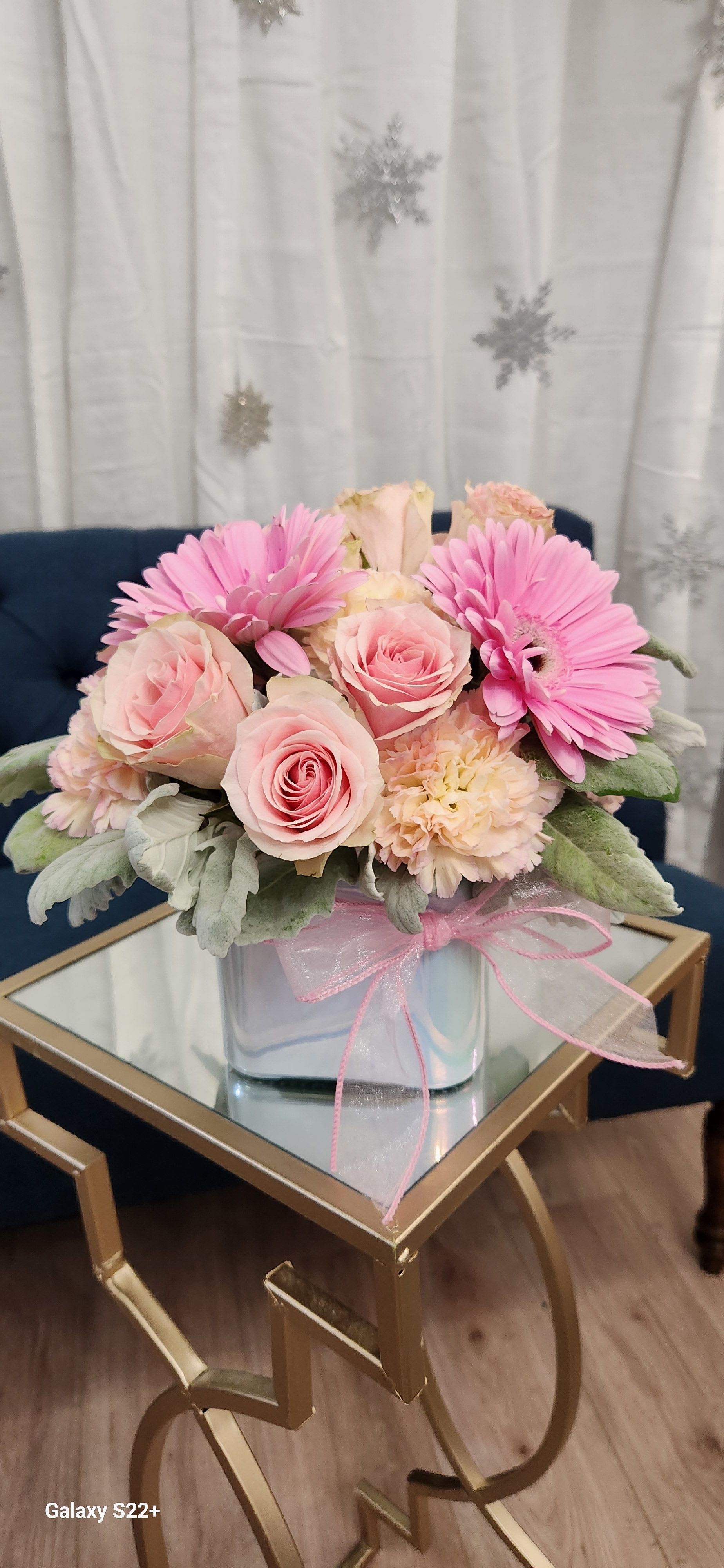 Pink roses and gerbera daisies in a clear glass vase with a pink ribbon