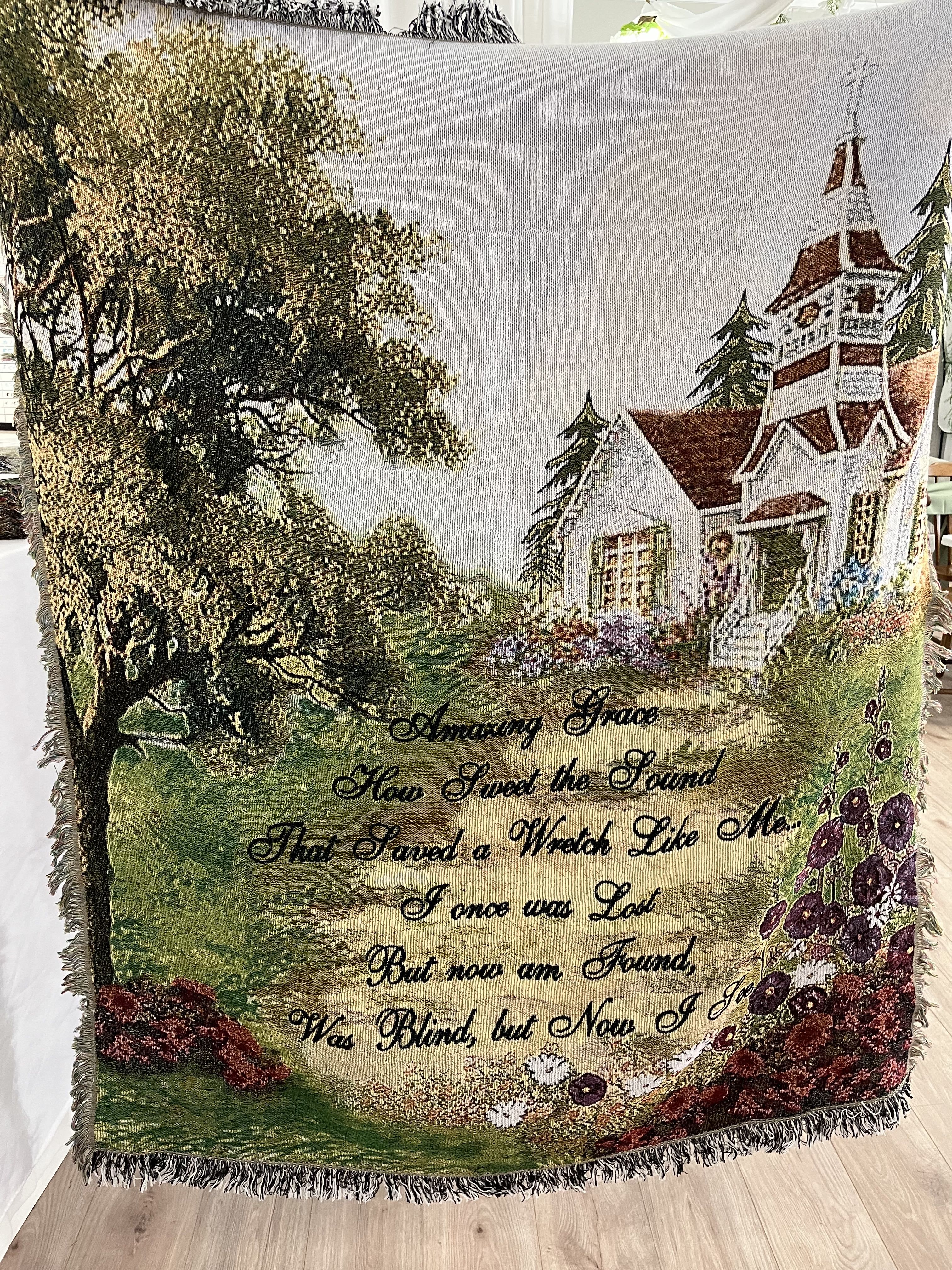 Decorative woven throw with a house, trees, and floral border