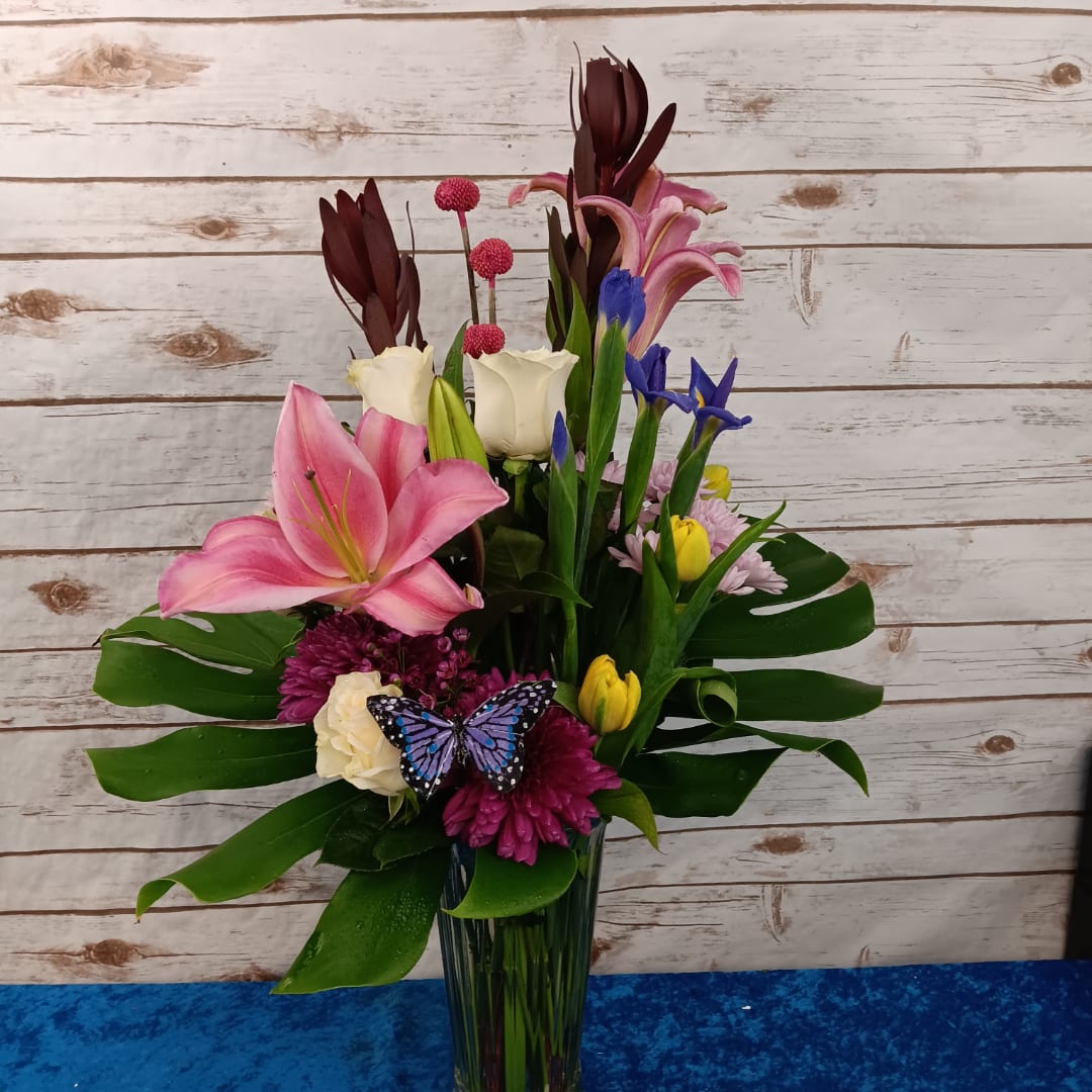 Mixed bouquet in a tall glass vase with pink lilies, roses, and blue flowers