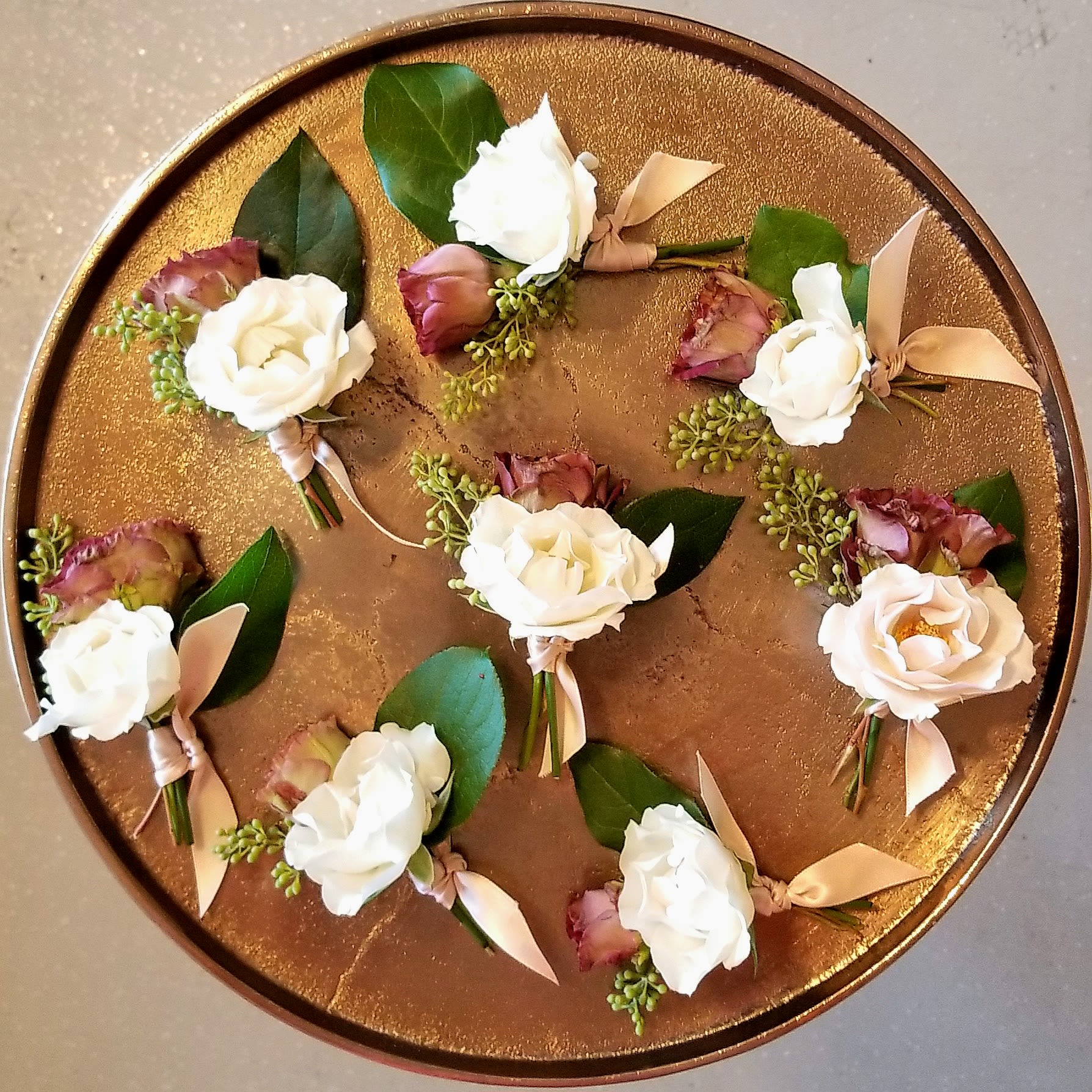 Small white rose boutonnieres arranged on a round gold tray