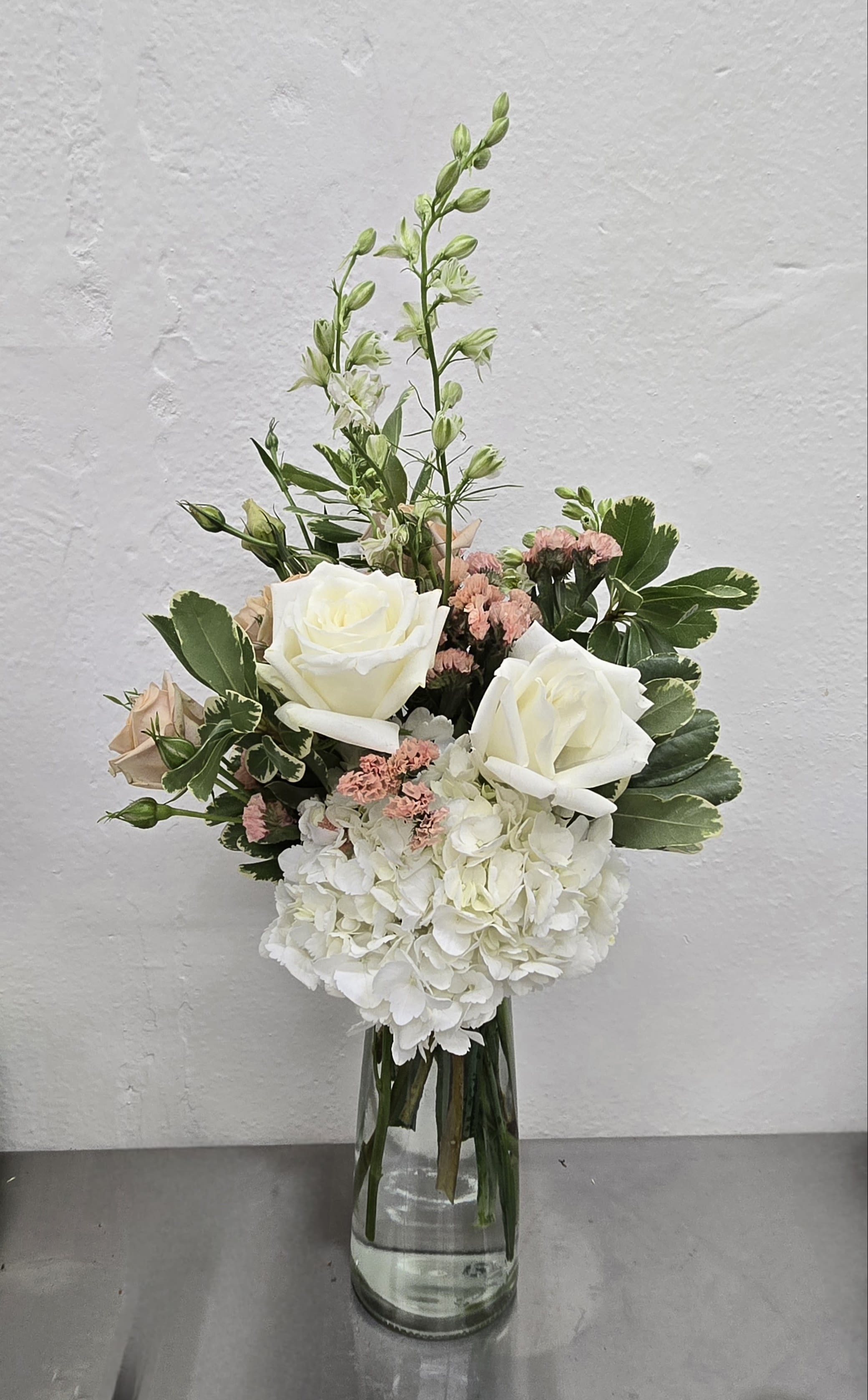 White roses and hydrangea in a clear glass vase with pink accents