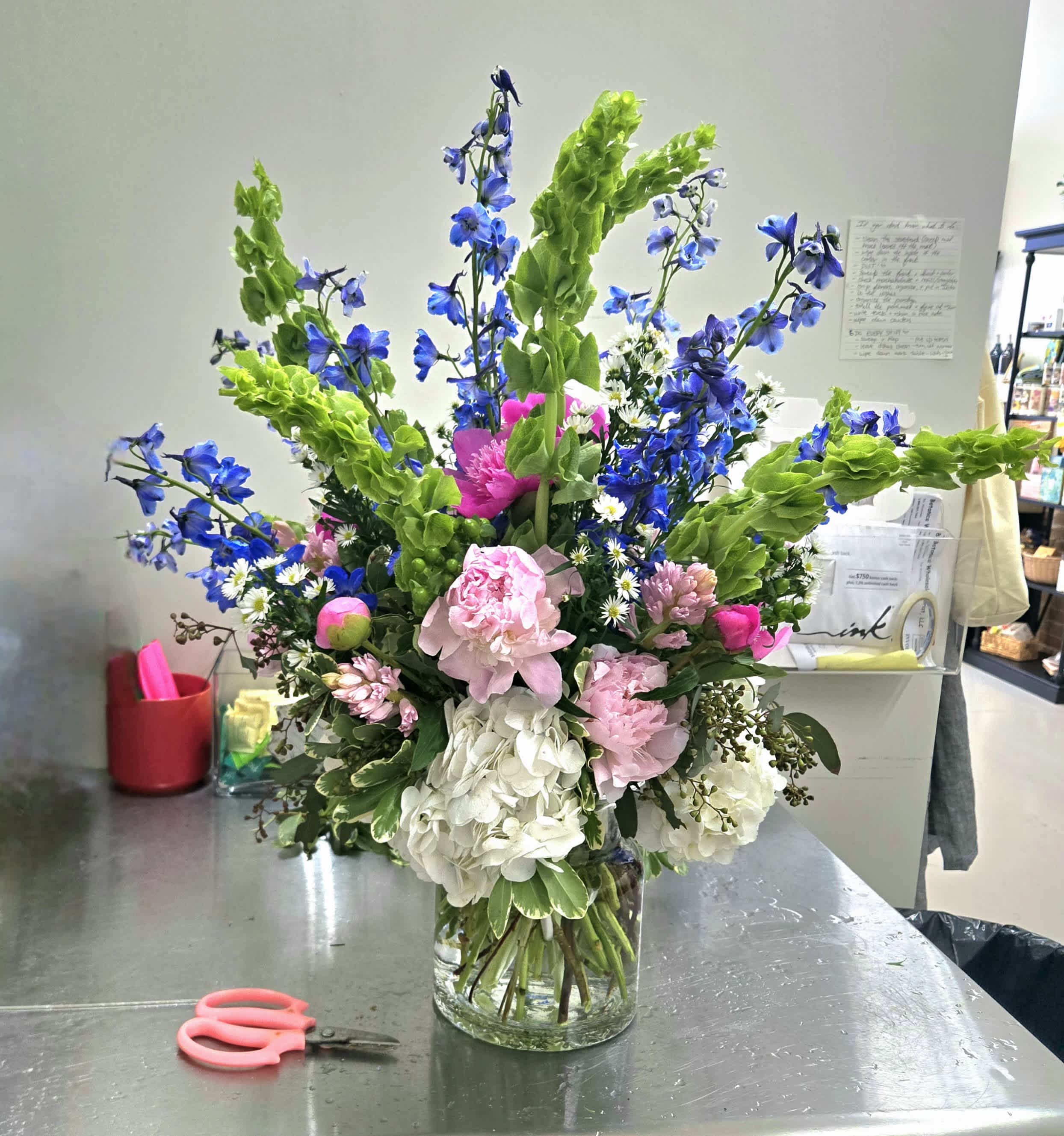 Tall mixed bouquet in a clear glass vase with pink, white, blue, and green flowers.