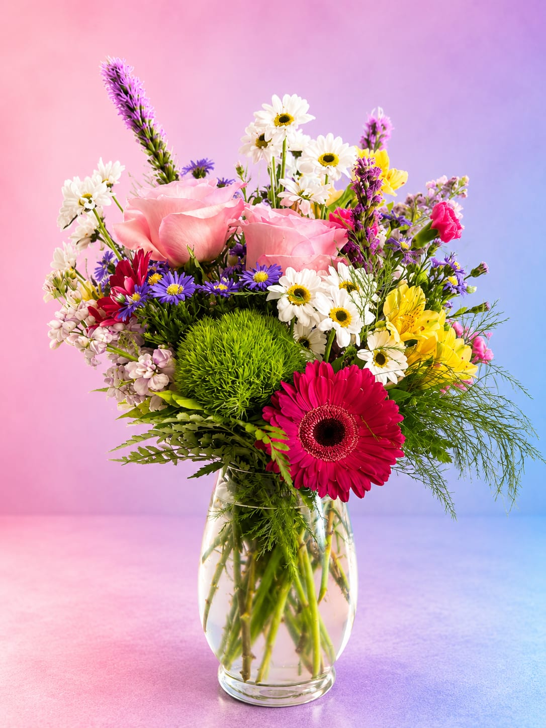 Mixed bouquet of pink roses, daisies, and gerbera in a clear glass vase