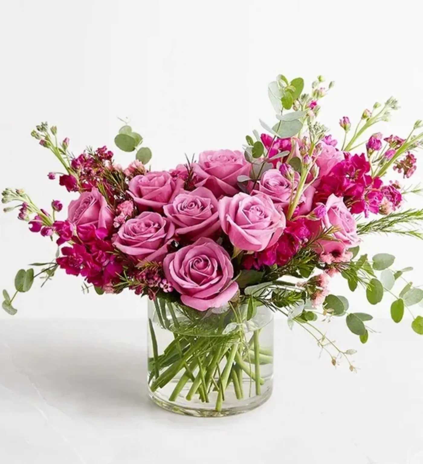 Pink roses and magenta flowers arranged in a clear glass vase