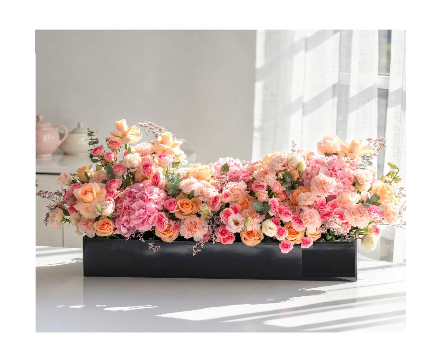 Low floral arrangement of pink and peach roses in a black rectangular container