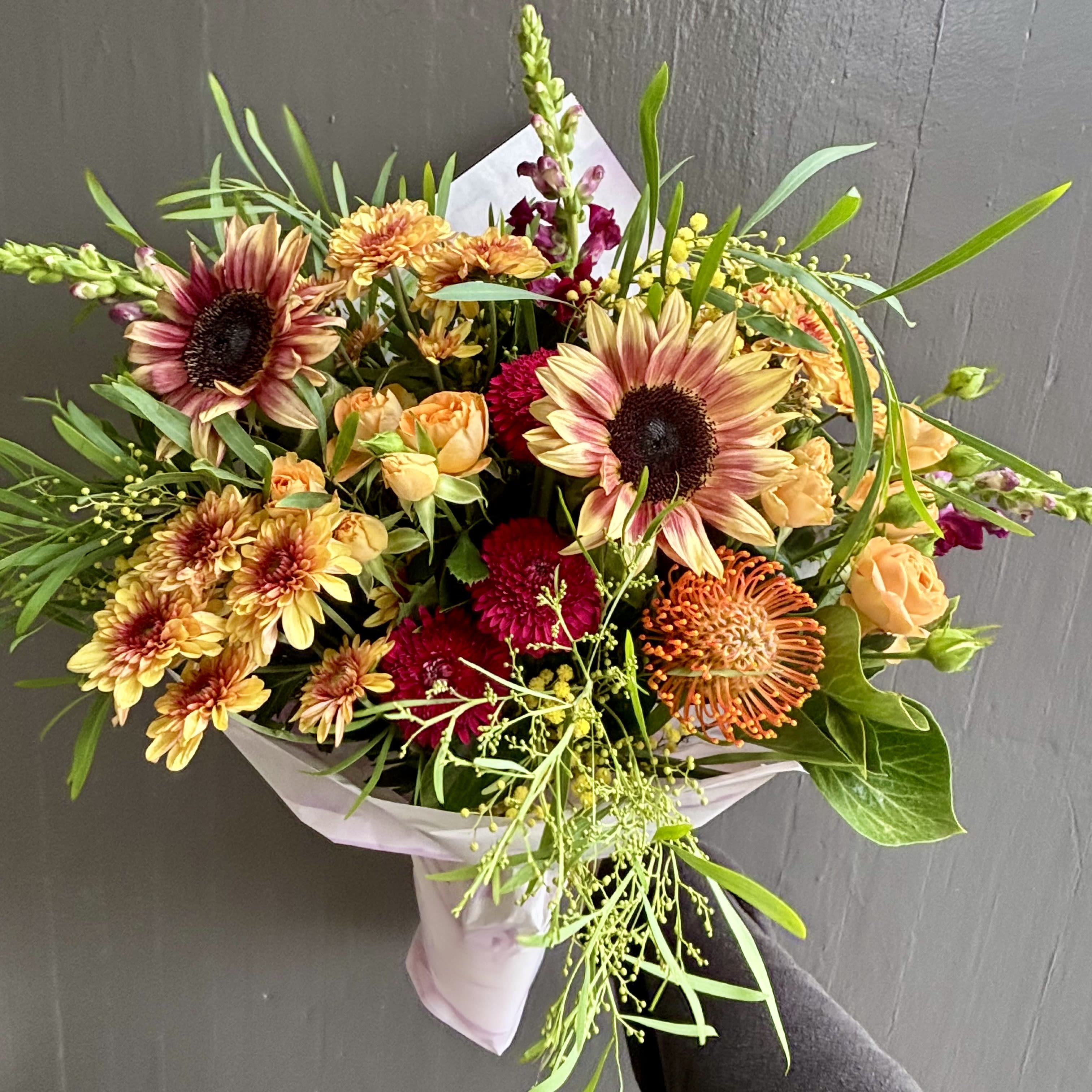 Mixed bouquet with sunflowers, roses, and chrysanthemums wrapped in pale paper