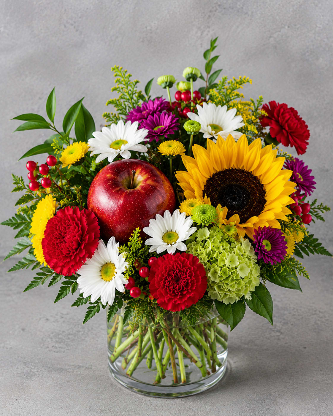 Class Act - Celebrate the people who make a difference every day with Class Act. This cheerful, handcrafted arrangement features radiant sunflowers, premium carnations, hydrangea, daisies, seasonal blooms, lush greenery, and a fresh red apple nestled among the flowers for a charming finishing touch. Whether you're welcoming a new school year, thanking a favorite teacher, recognizing a dedicated staff member, or simply brightening someone's day, this vibrant design is sure to leave a lasting impression. Flower varieties and colors may vary based on seasonal availability while maintaining the overall style, color palette, and value of the arrangement.