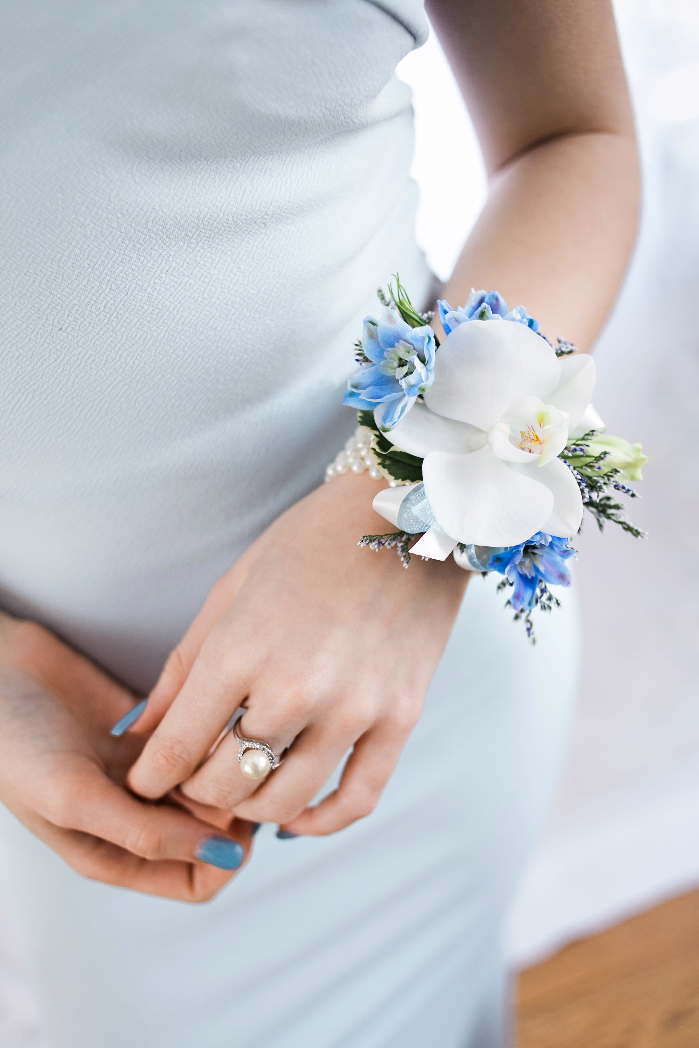 Wrist corsage with white orchid and blue flowers on a pearl bracelet worn with a light blue dress