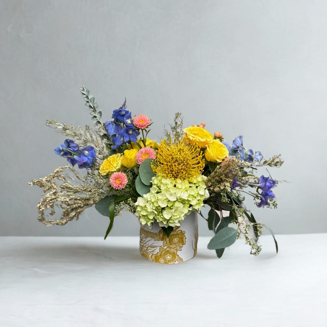 Colorful bouquet in a white floral vase with yellow, blue, pink, and green blooms