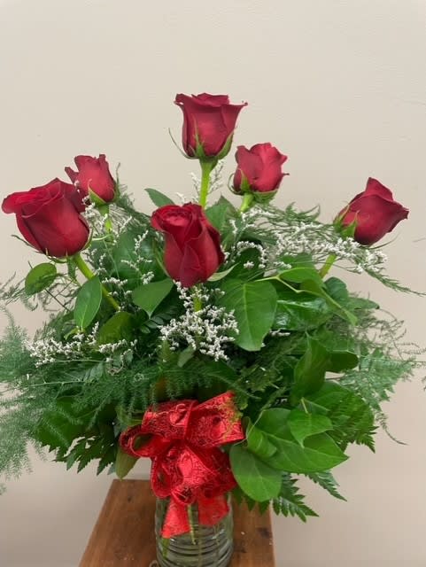 Red roses arranged in a glass vase with a red ribbon