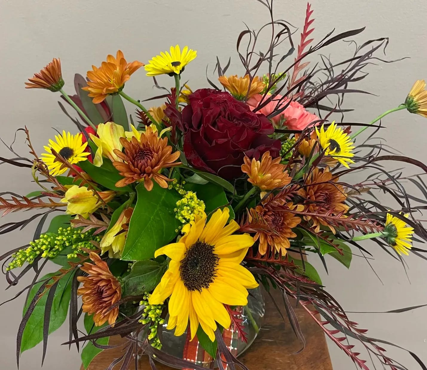 Mixed bouquet with a red rose, sunflowers, and orange daisies in a glass vase