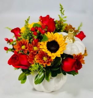 Bouquet of red roses, sunflowers, and orange mums in a white pumpkin container
