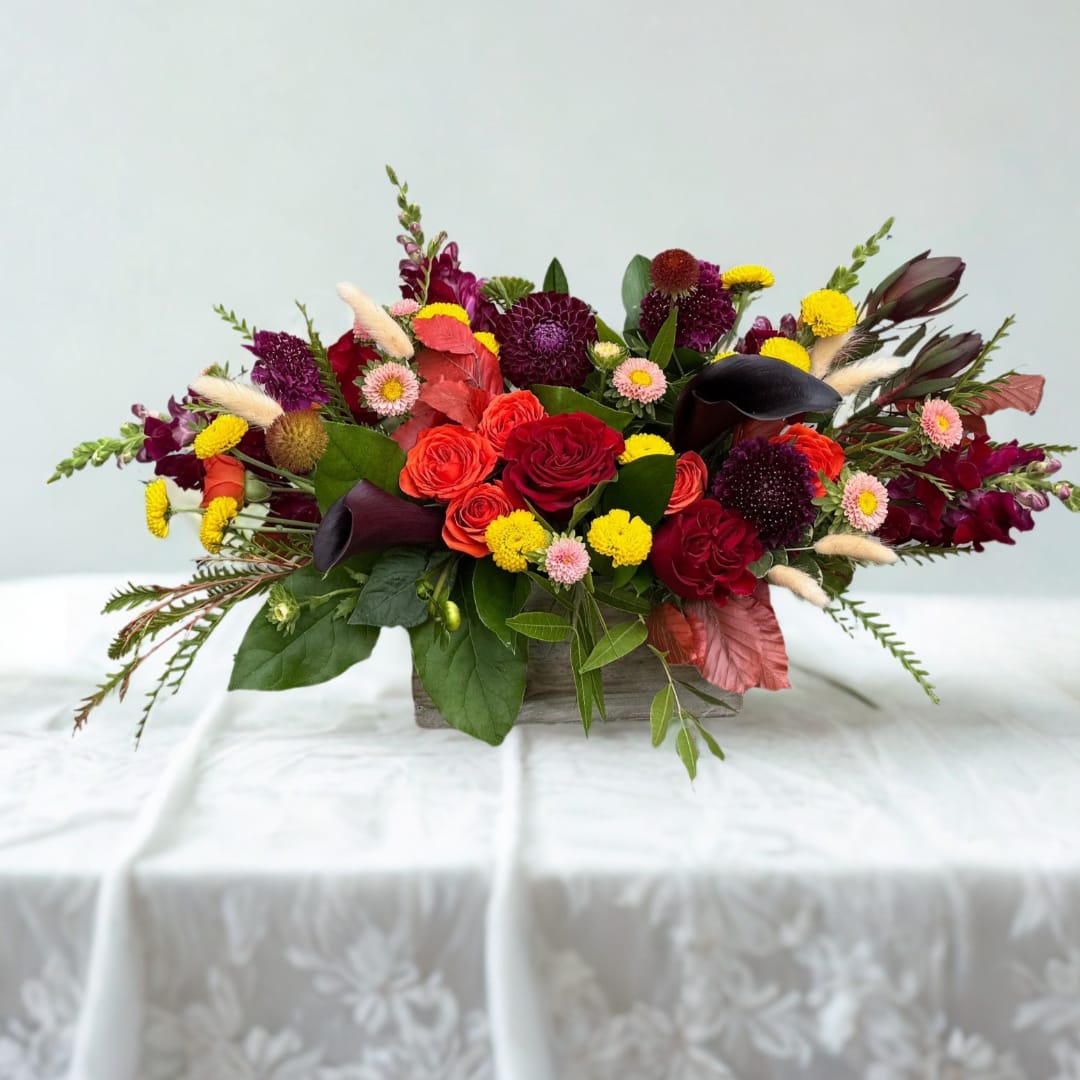 Low floral centerpiece with red roses, calla lilies, and yellow accents in a wooden container