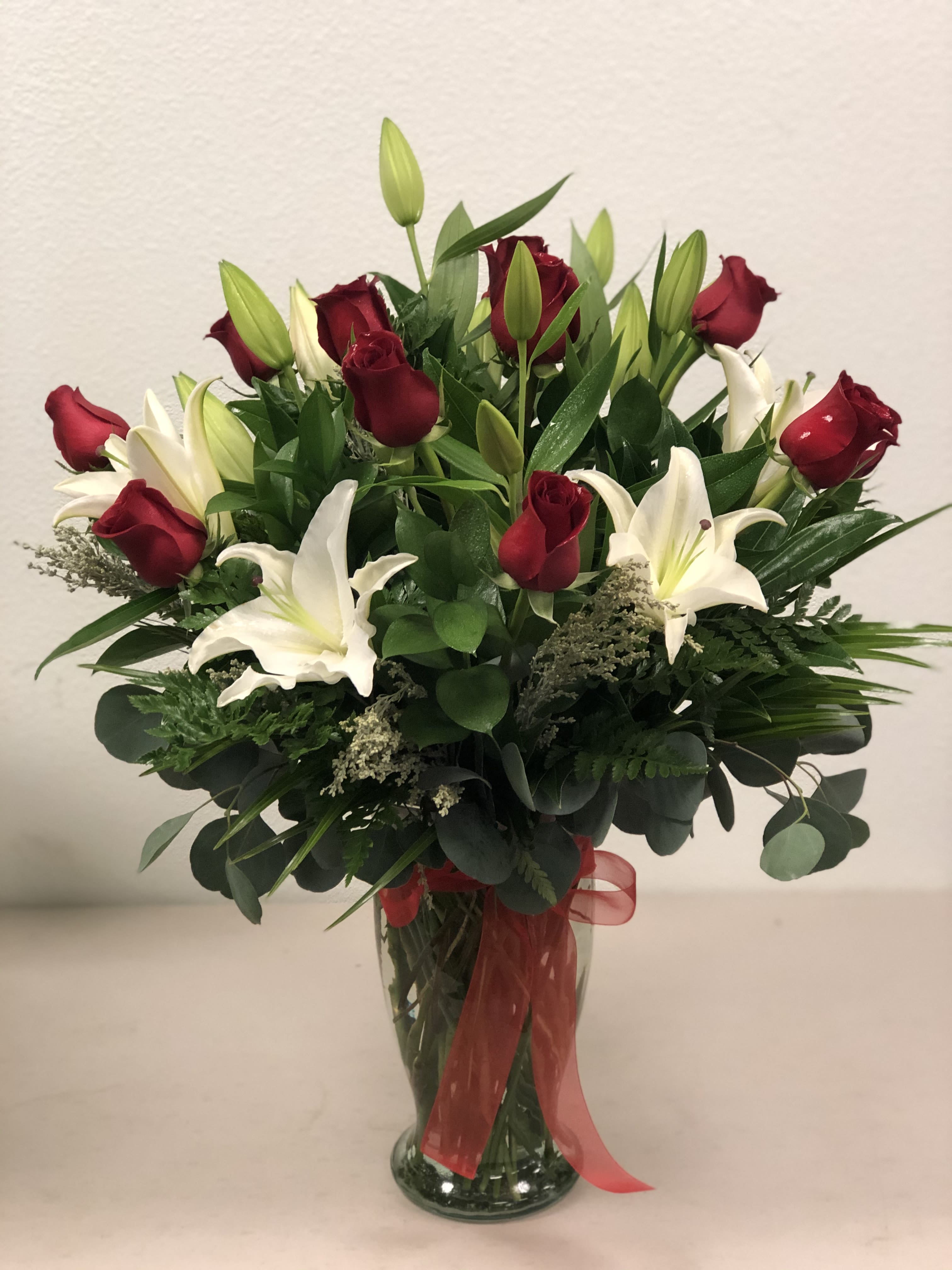 Red roses and white lilies in a clear glass vase with a red ribbon