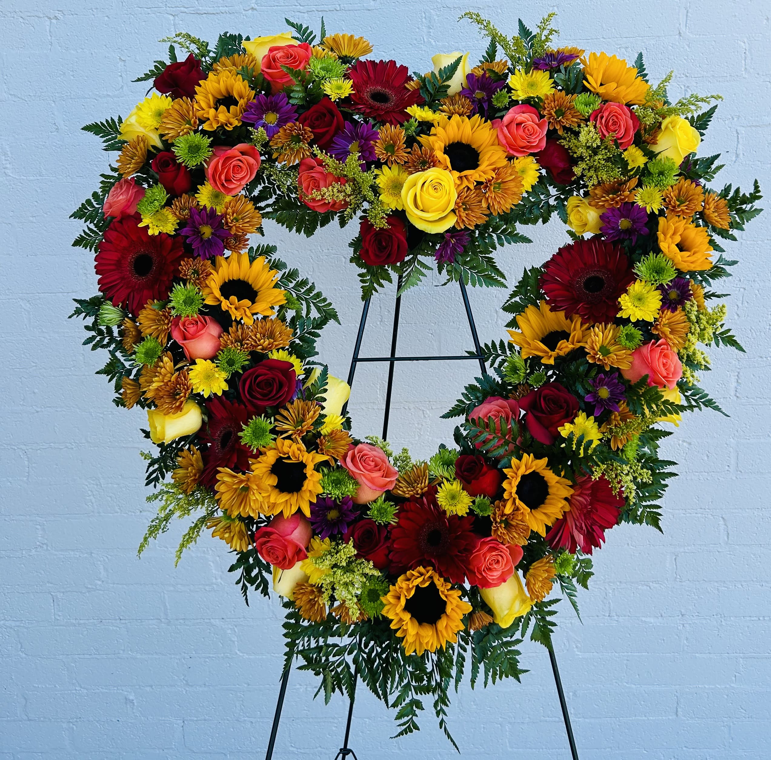 Heart-shaped floral arrangement with roses, sunflowers, and mixed blooms on an easel