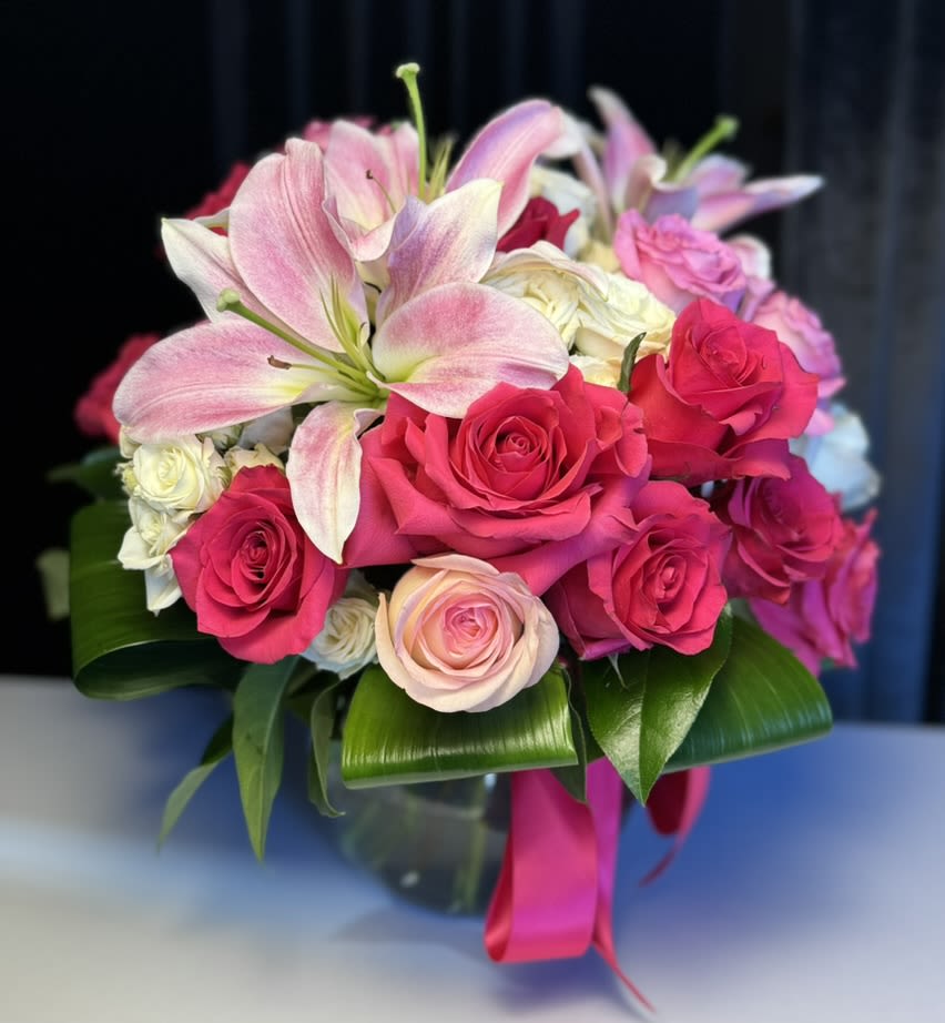 Pink lilies and roses arranged in a glass vase with a ribbon