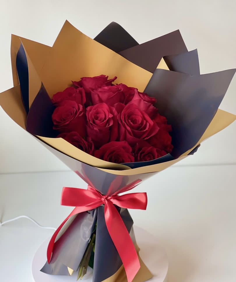Bouquet of red roses wrapped in gold and dark paper with a red ribbon