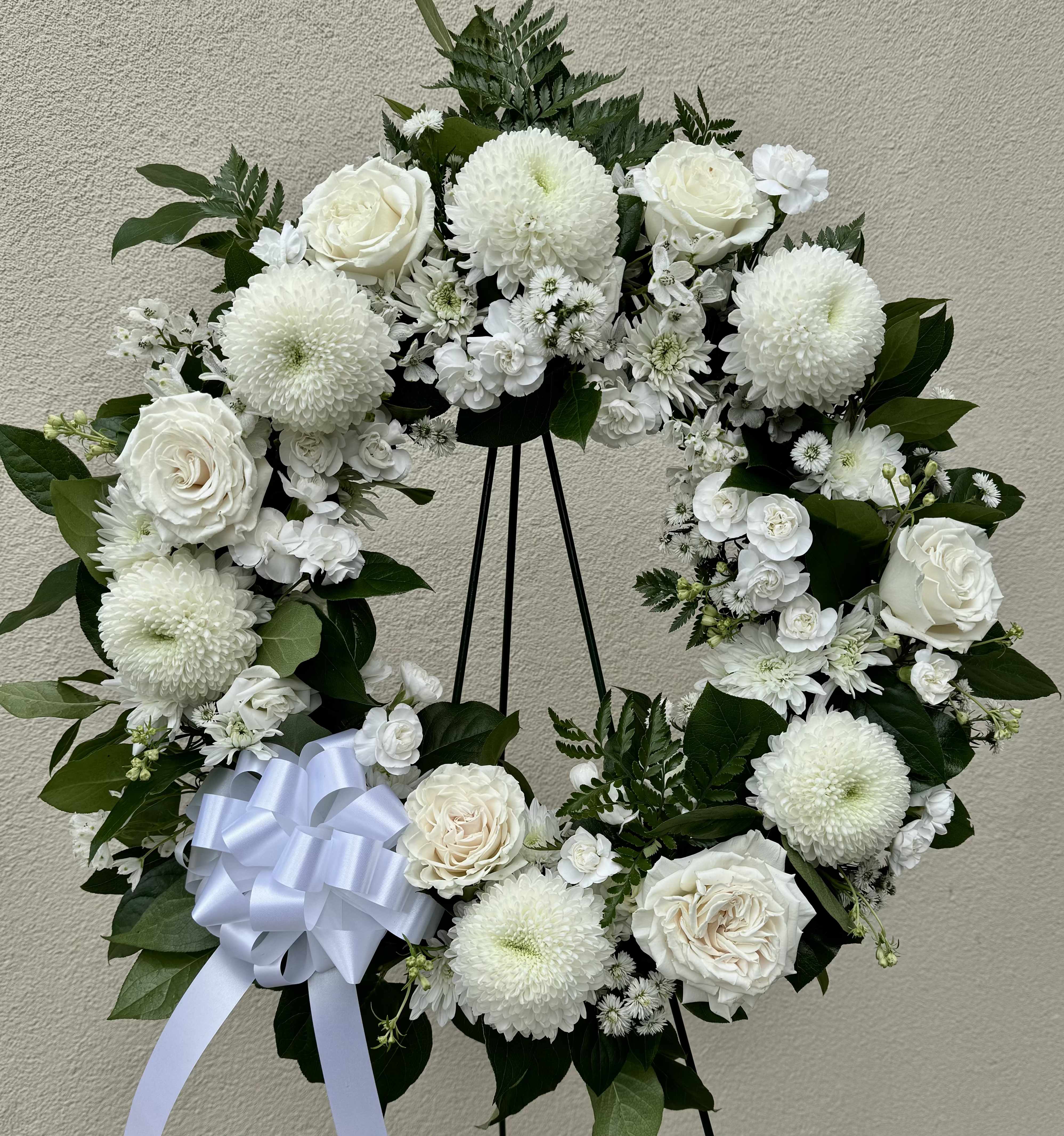 White floral wreath with roses and mums on a black stand