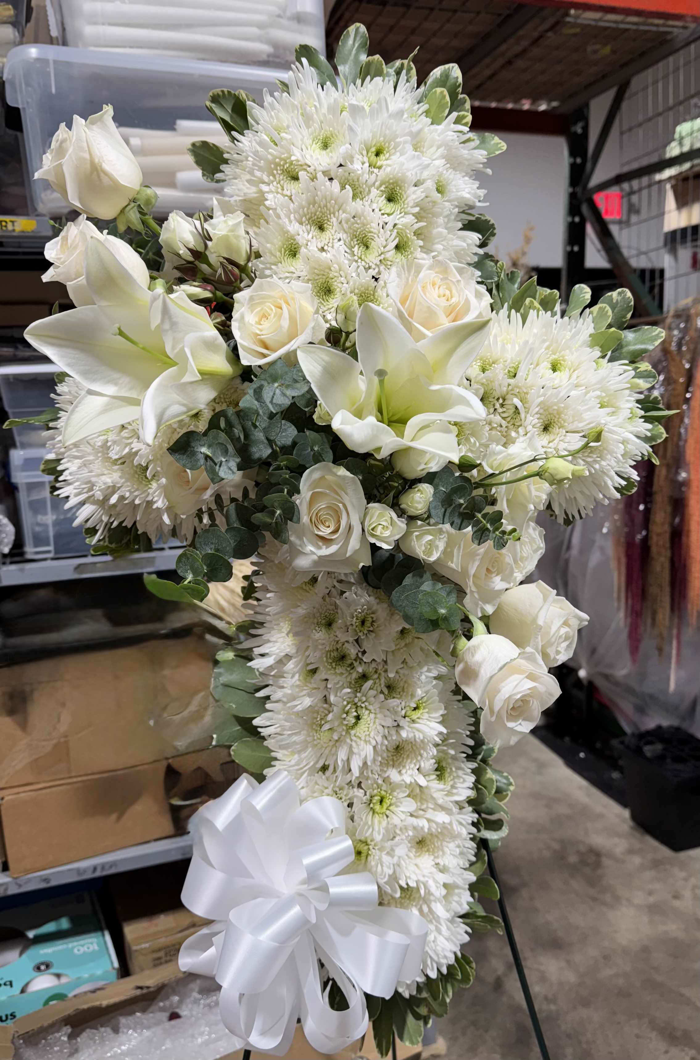 White roses, lilies, and chrysanthemums arranged in a tall spray with a white ribbon.