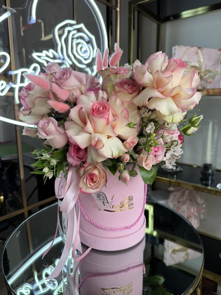 Pink and cream roses arranged in a round pink box with ribbon.
