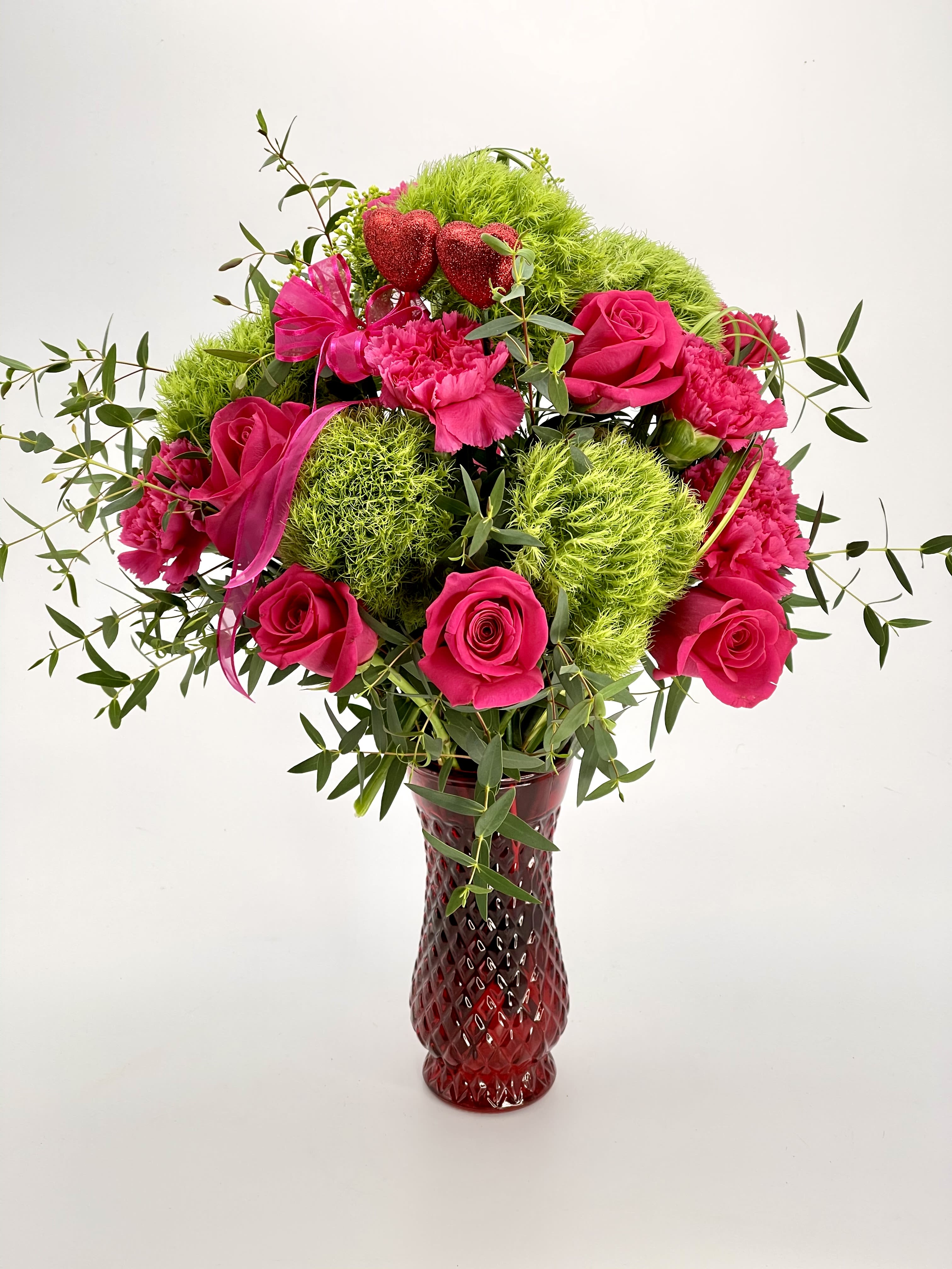 Sweetheart Garden Bouquet  - A charming and romantic arrangement featuring vibrant hot pink roses and carnations, playful green trick dianthus, and delicate accents of greenery, beautifully presented in a rich red glass vase with sparkling heart details. Perfect for celebrating love, friendship, or any heartfelt occasion.