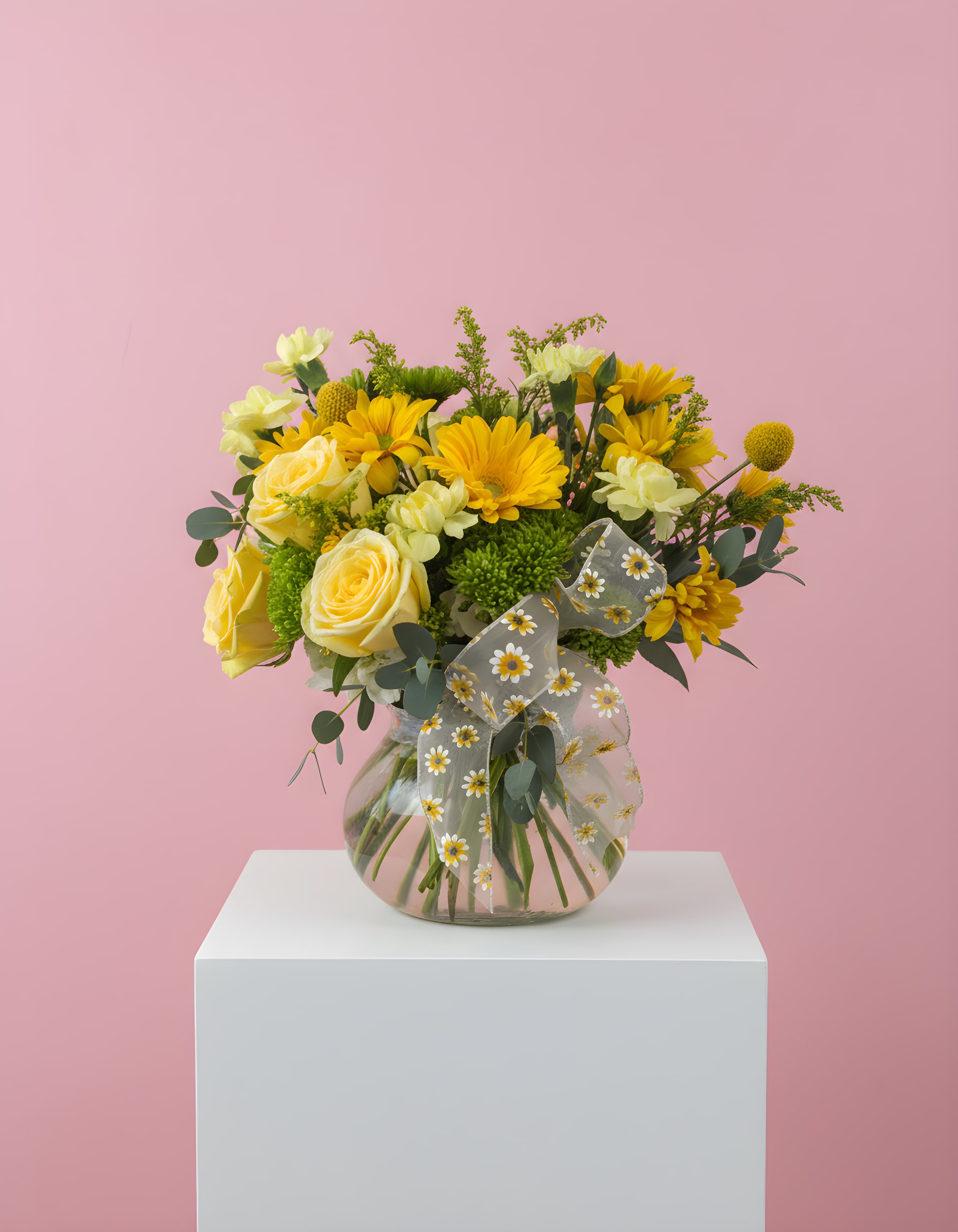 Yellow flowers in a clear glass vase with a sheer daisy ribbon