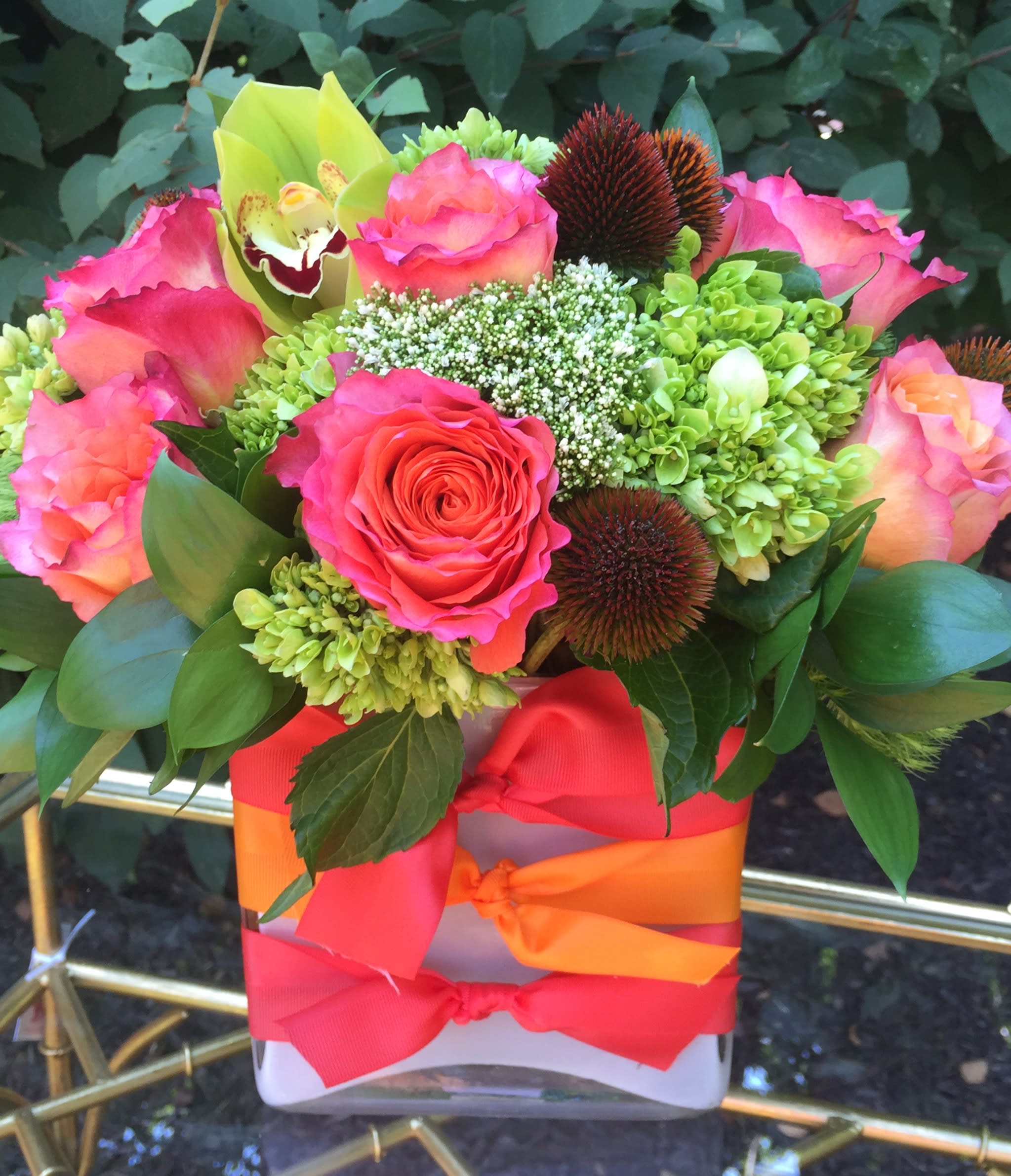 Rainbow Sherbert - Free Spirit roses, cone flower, white trick, fancy green and green orchids arranged in a white vase with peach and orange bow ties.  **Deluxe Shown** Tax free. Same day hand delivery.