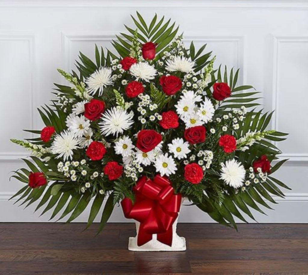 Red roses and white daisies in a white vase with a red bow