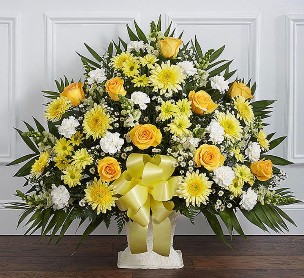 Yellow and white floral spray with a ribbon on a pedestal stand