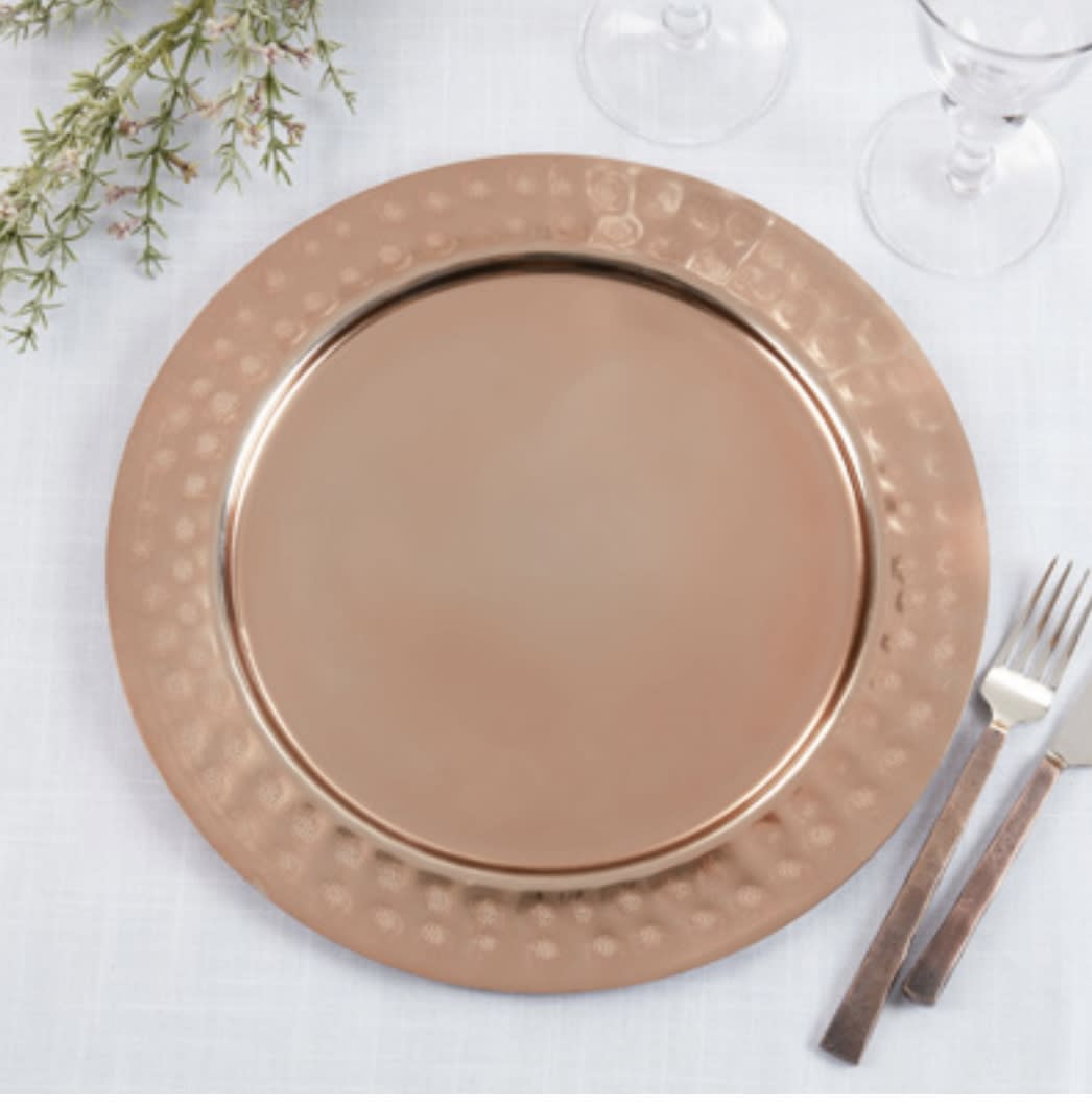 Rose-gold charger plate on a white table setting with glassware and cutlery