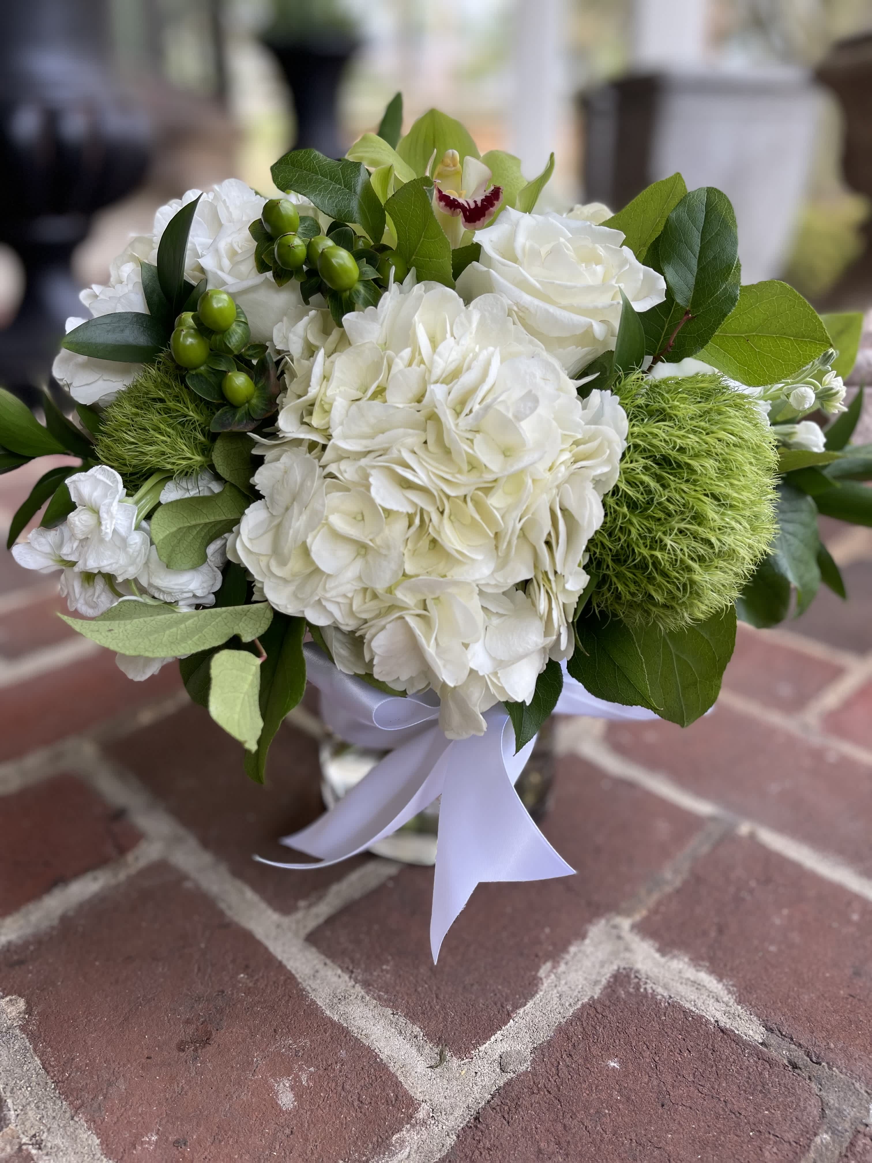 Calming Serenity - Calming Serenity – Soothing White and Green Floral Arrangement | Wilmington, DE Local Florist  Discover tranquility with Calming Serenity, an elegant floral arrangement thoughtfully designed by Petals Flowers and Fine Gifts, your trusted local florist in Wilmington, Delaware. This serene bouquet features lush white hydrangea, classic white roses, fresh green hypericum berries, vibrant green trichelium, and a striking green orchid, all beautifully arranged in a clear glass vase. Finished with a delicate white satin ribbon, this arrangement is perfect for expressing sympathy, gratitude, or simply bringing a peaceful touch to any room.  We offer same-day flower delivery in Wilmington, DE, and to nearby areas including Hockessin, Newark, Glen Mills, Chadds Ford, Christiana, and Landenberg.  Why Choose Us:  * Locally owned and operated florist serving Wilmington, Delaware, and surrounding communities * Custom, hand-crafted floral designs made with premium quality flowers * Commitment to exceptional customer service and satisfaction guarantee * Enjoy tax-free flower delivery on all orders Order Calming Serenity today from Petals Flowers and Fine Gifts and share the gift of peace and beauty with someone special.