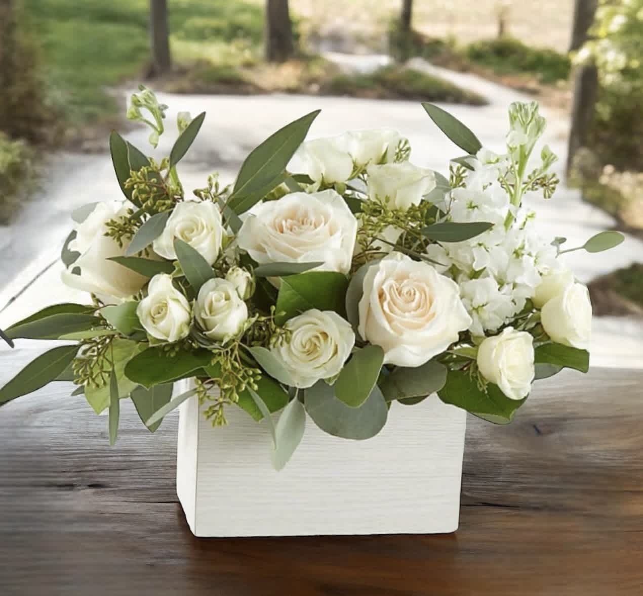 White roses arranged in a white rectangular box with greenery
