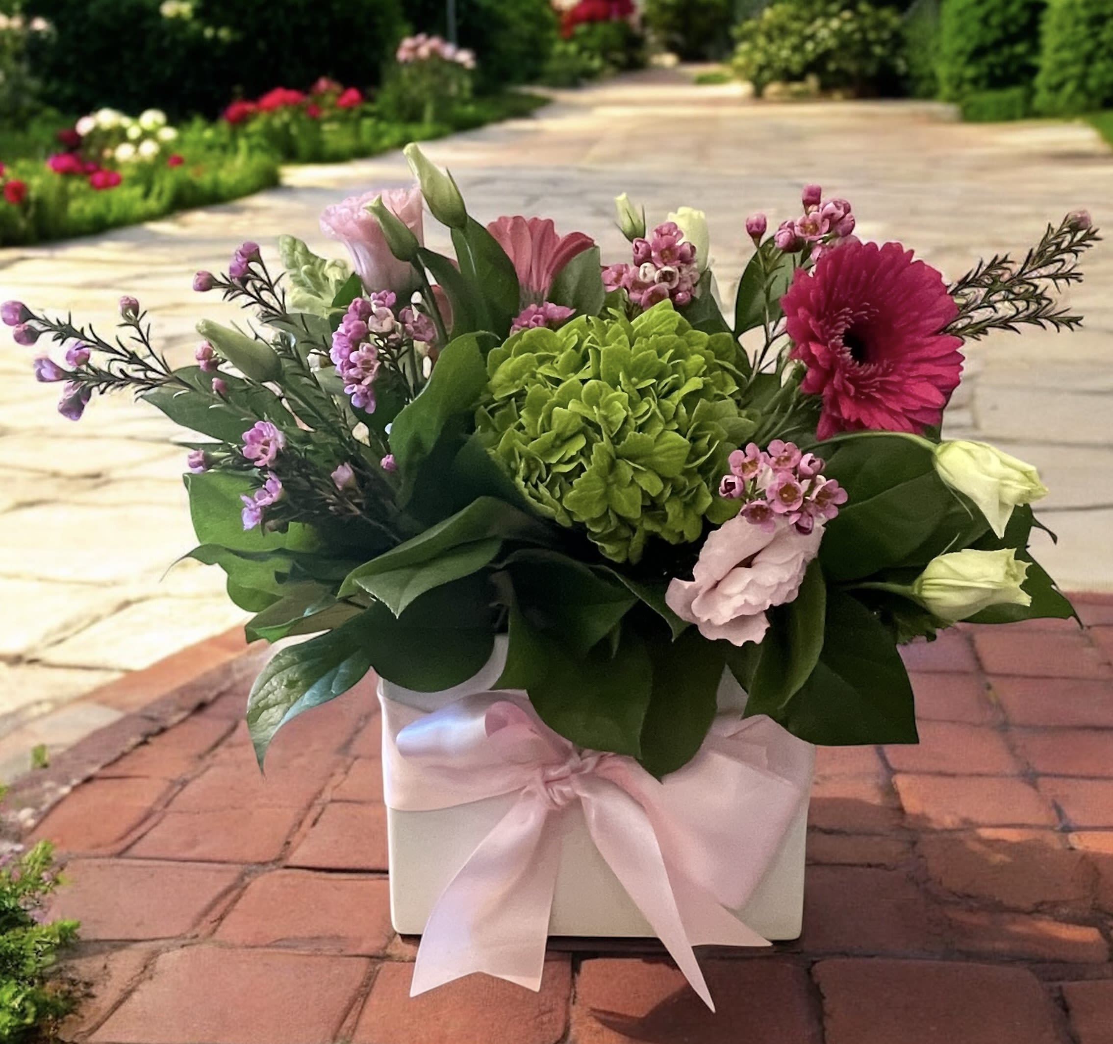 Spring Blush - Spring Blush – Fresh Flower Arrangement | Wilmington, Delaware Florist  Celebrate the beauty of spring with Spring Blush, a stunning floral arrangement handcrafted by our expert designers at Petals Flowers and Fine Gifts in Wilmington, Delaware. This vibrant design features lush green hydrangea, bold dark pink gerber daisies, delicate pink lisianthus, and charming pink waxflower, all artfully arranged in a modern white cube vase tied with a soft satin pink ribbon.  Perfect for birthdays, anniversaries, new baby celebrations, or simply brightening someone’s day, Spring Blush brings a pop of cheerful color to any space. We offer same-day flower delivery in Wilmington, DE and surrounding areas, including Hockessin, Newark, Glen Mills, Chadds Ford, Kennett Square, Christiana, and Landenberg.  Order online or visit our Wilmington flower shop for fresh, custom floral arrangements designed with care and backed by our satisfaction guarantee.