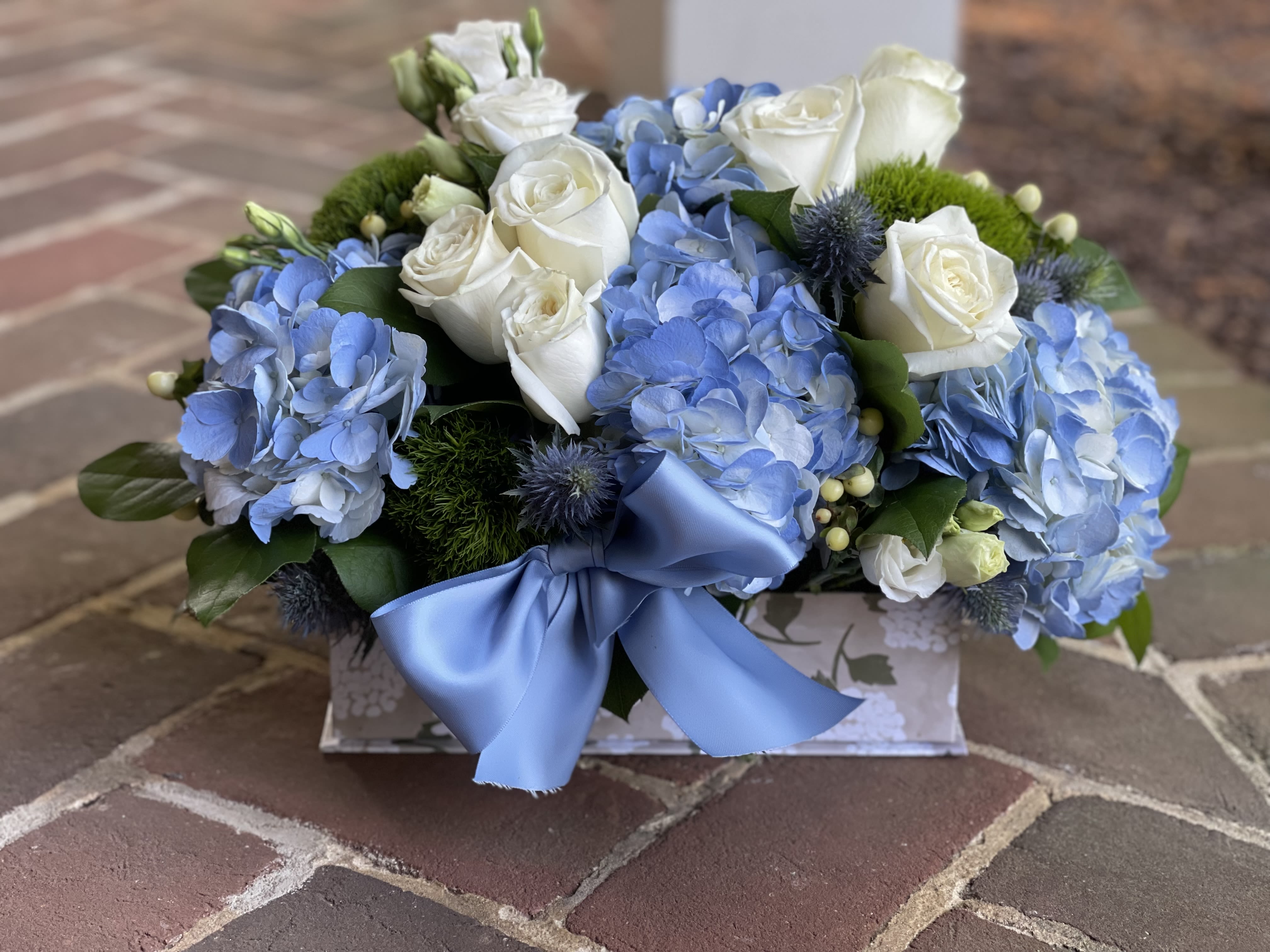 Blue Serenity - A calming blend of blue hydrangeas, white roses, and accent florals nestled in lush greenery, all arranged in a decorative box with a soft blue satin bow. Tax free. Same-day hand delivery.  We are a local florist in Wilmington, Delaware that provides the best delivery of fresh flowers on the same day. We also offer next day delivery. Our flower shop services the Wilmington and Newark Delaware areas as well as south eastern PA. We are a flower shop near you that is tax free and provides hand delivered flowers. We offer funeral, sympathy, anniversary, birthday, holiday, Mother's Day, Valentine's Day and rose arrangements and flowers for all occasions. Petals is a full service florist that offers the best online flowers and fresh flower arrangements. You can send flowers from our flower shop to Wilmington, New Castle, Newark, Hockessin, Chadds Ford, Kennett Square and other local cities near us. 
