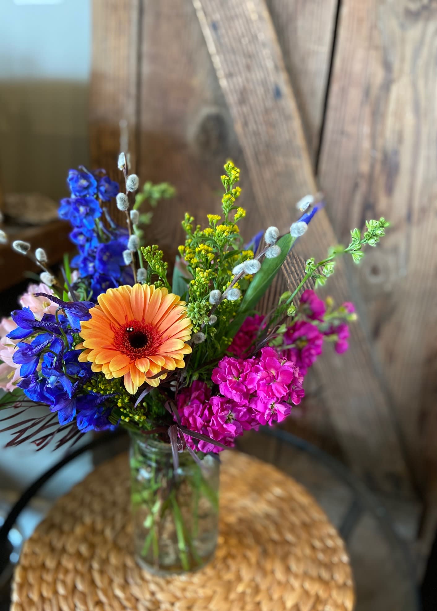 Colorful arrangement with orange gerbera, blue delphinium, and pink stock in a clear glass vase