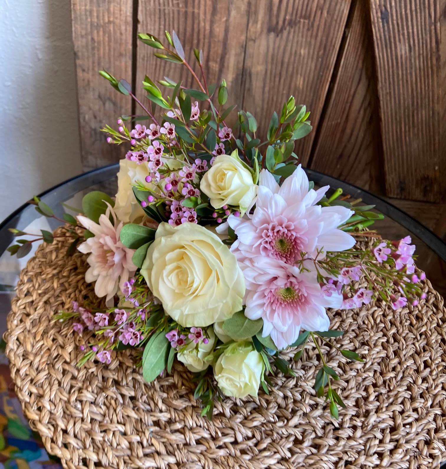 Low arrangement of cream roses and pale pink mums with tiny pink blossoms on a woven mat